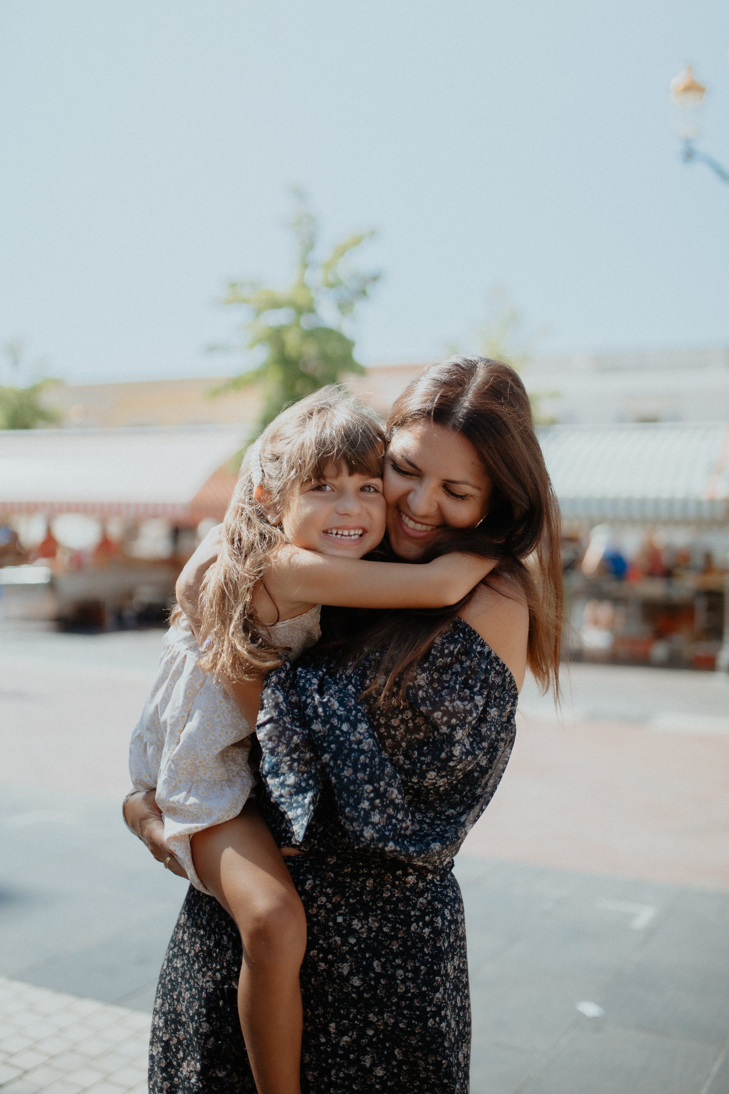 A woman holding a young girl in her arms while they hug outdoors on a sunny day.
