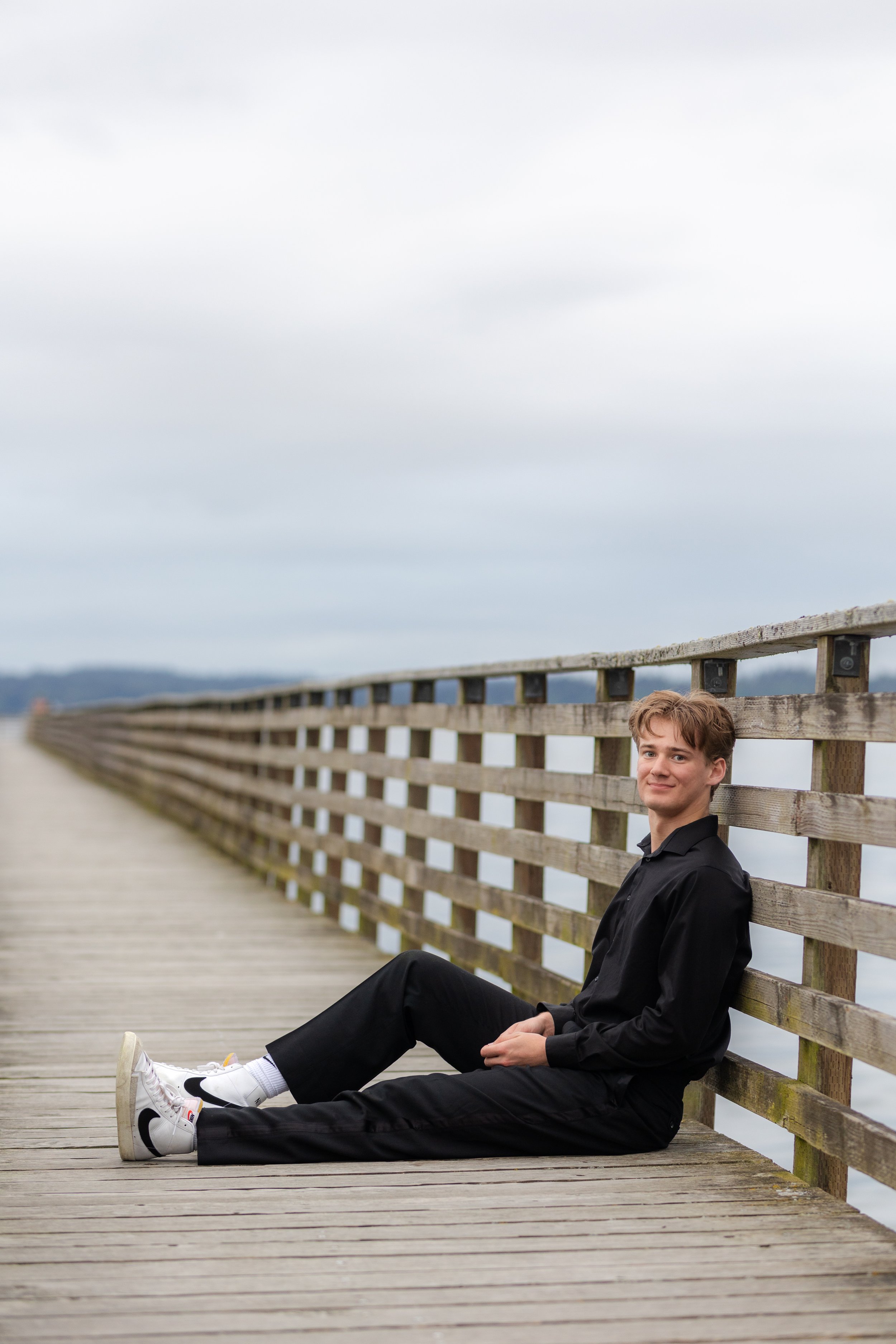 Senior picture of a boy sitting on the Indianola Pier in Indianola, WA