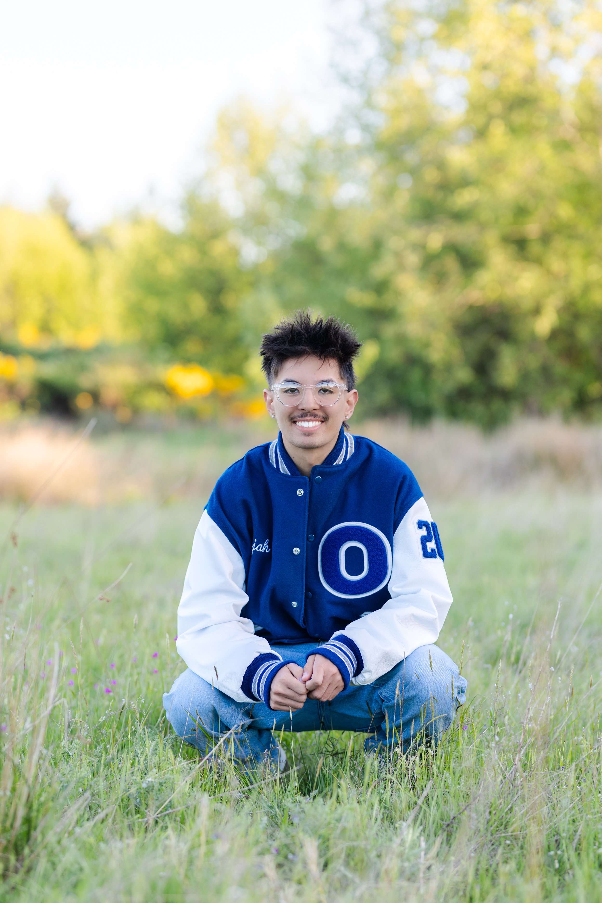 Senior picture of an Olympic High School senior in their letterman jacket at a Silverdale field