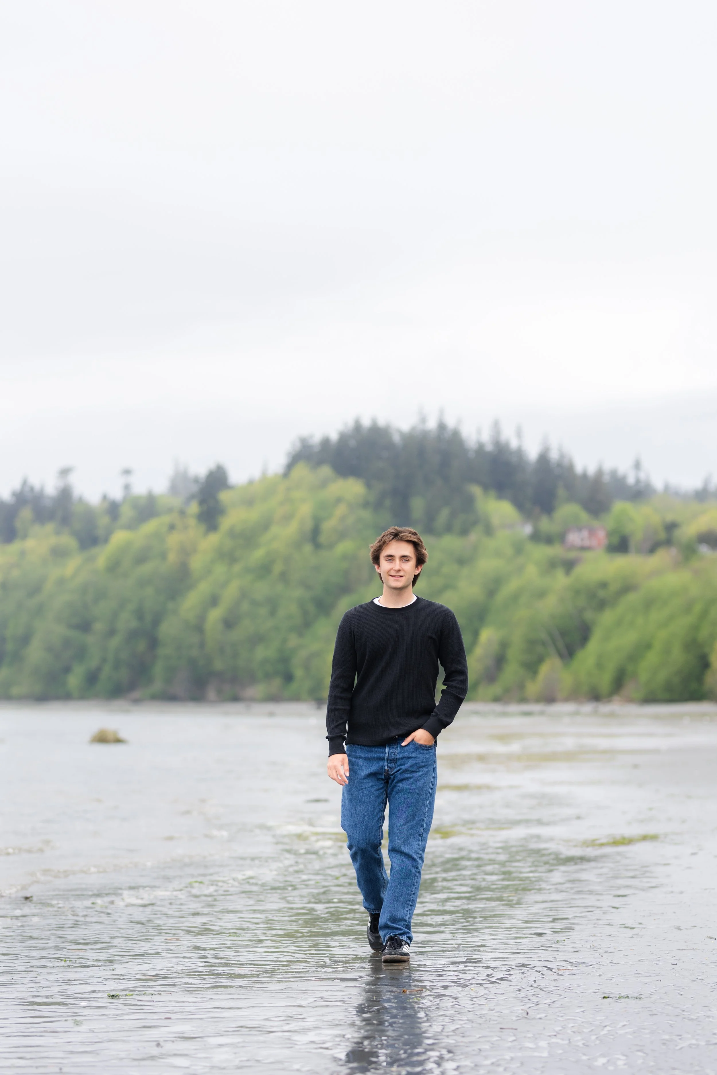 Senior picture of a boy walking along a beach on a cloudy day in North Kitsap, WA