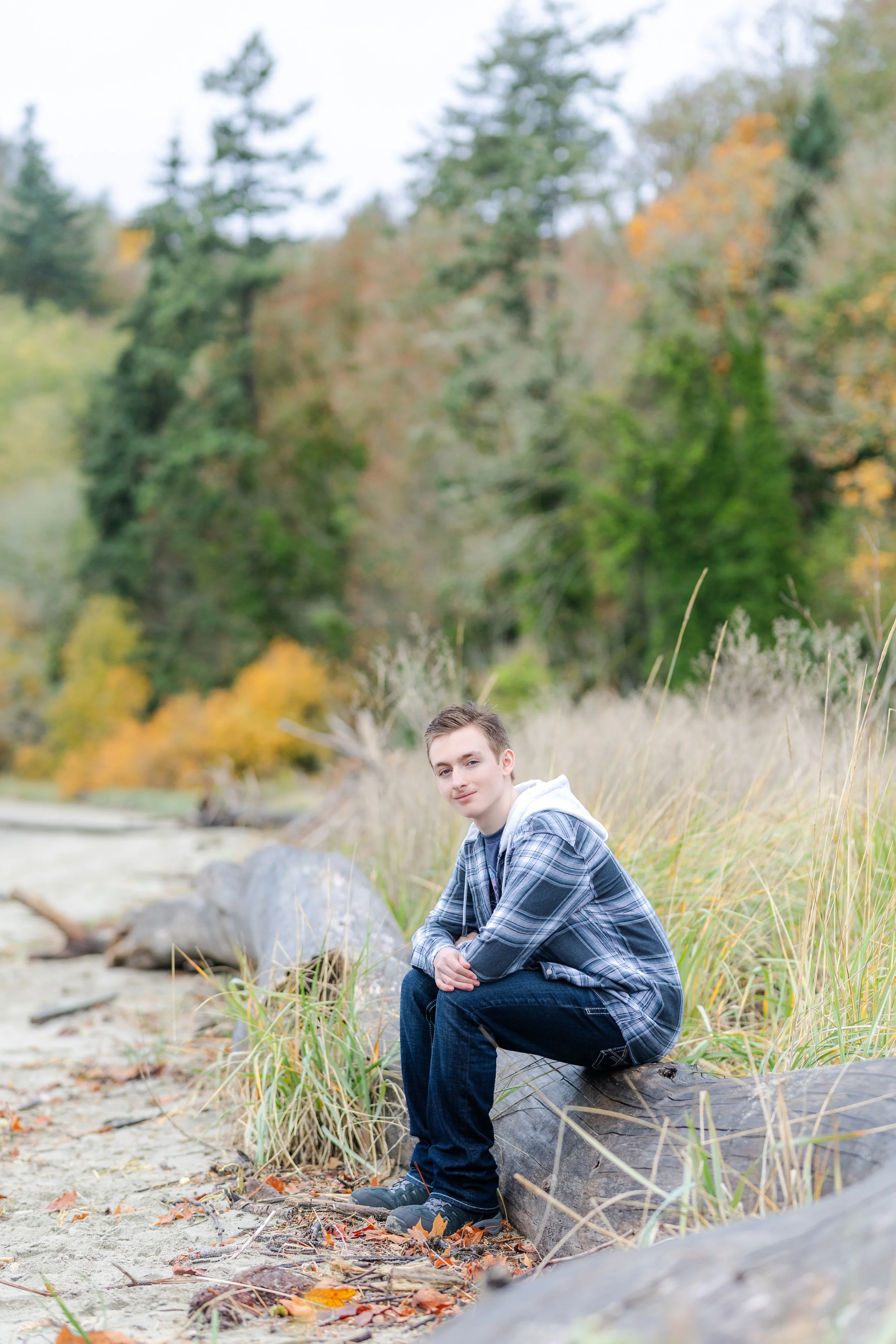 Port Orchard senior picture of senior sitting on driftwood at a beach with fall colors behind him