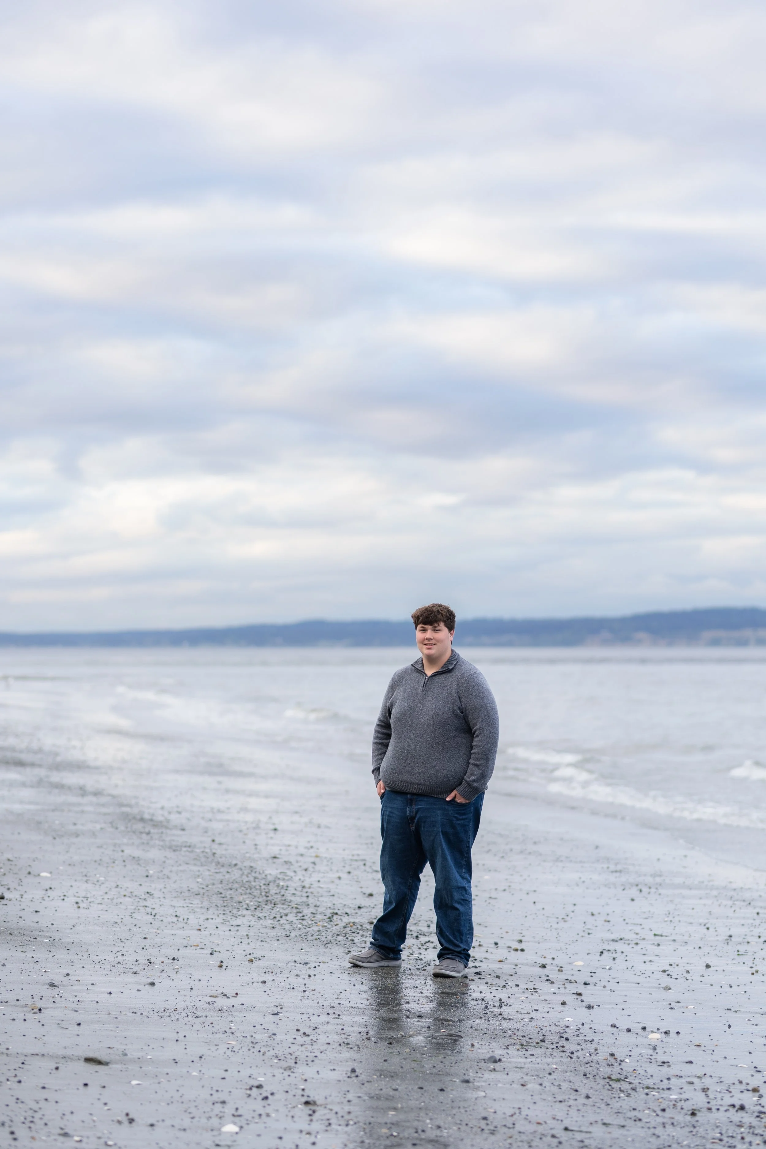 Cloudy spring senior photo taken of a boy near the water in North Kitsap