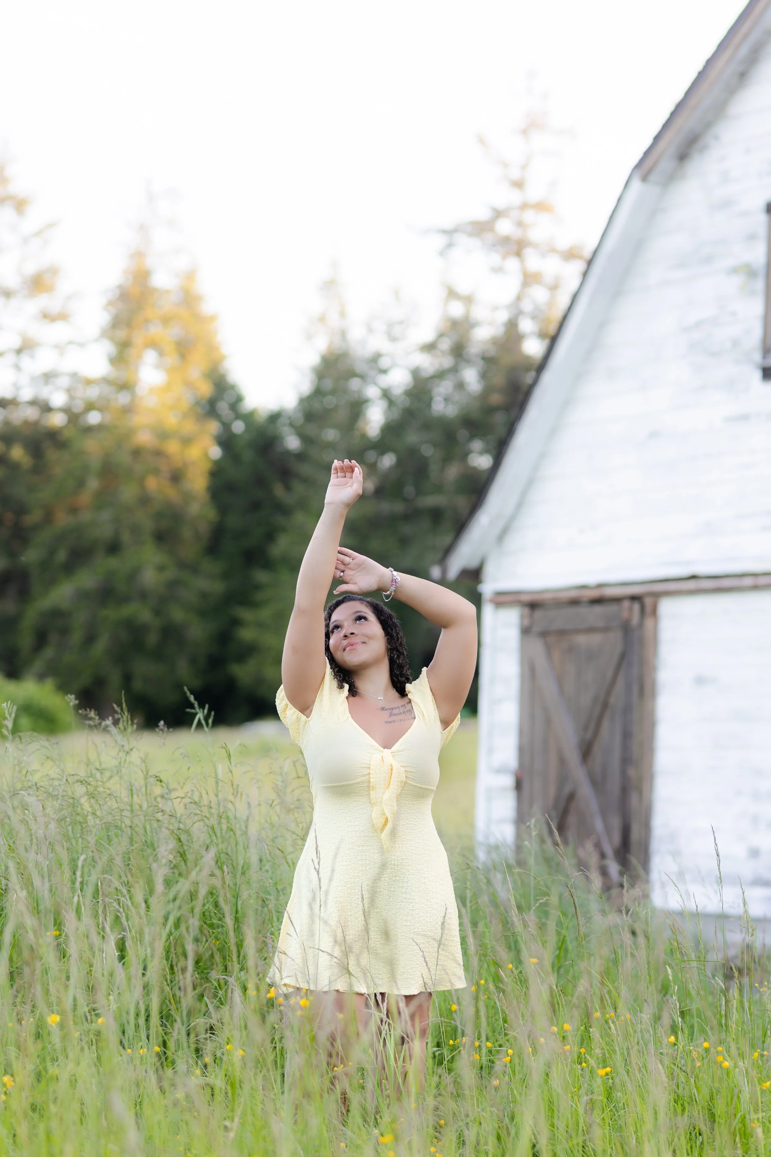 Senior picture in Kitsap of a girl in a yellow dress in grass in front of a white barn