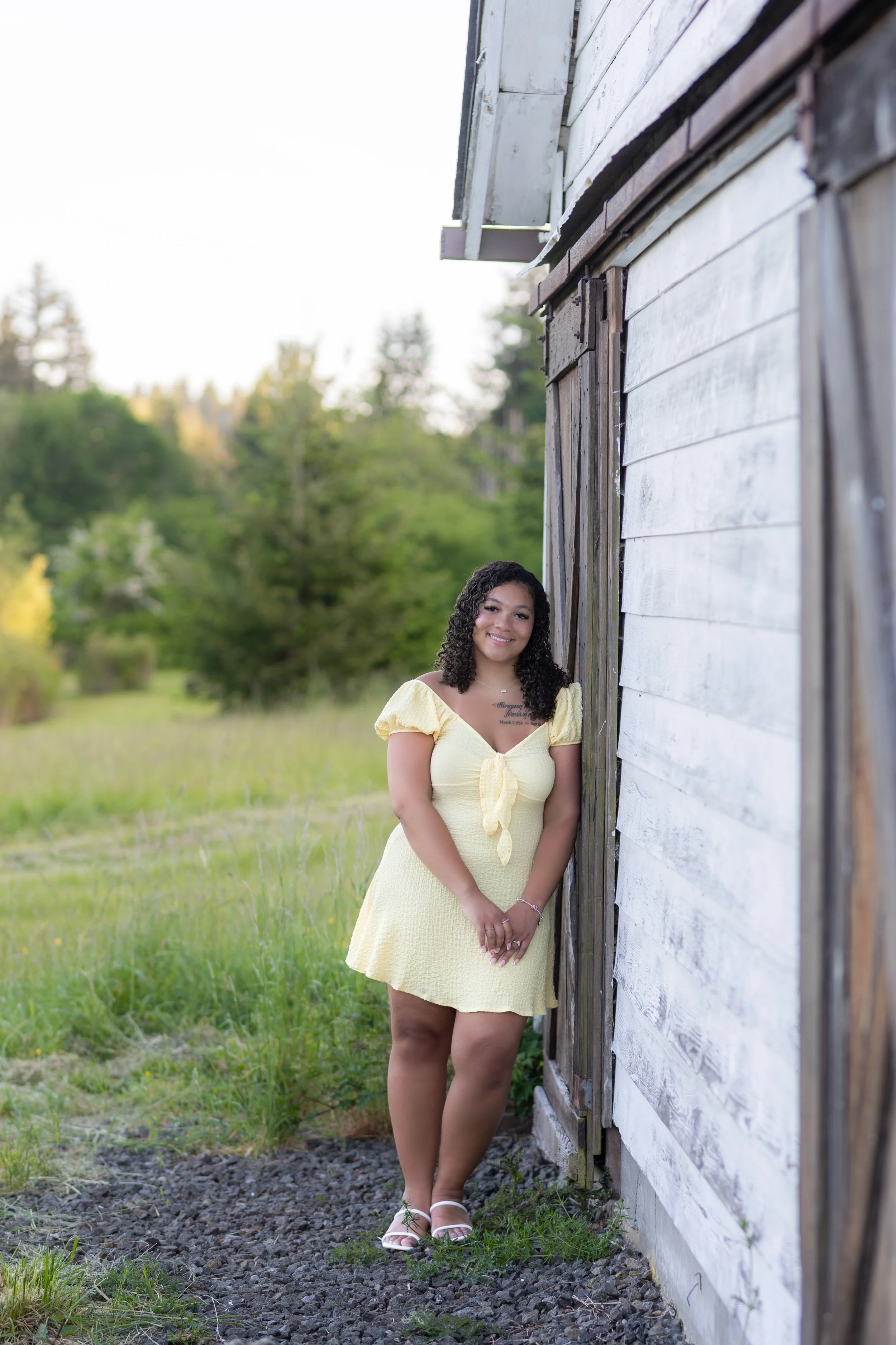 Kitsap senior picture of a girl in a yellow dress leaning against a white barn