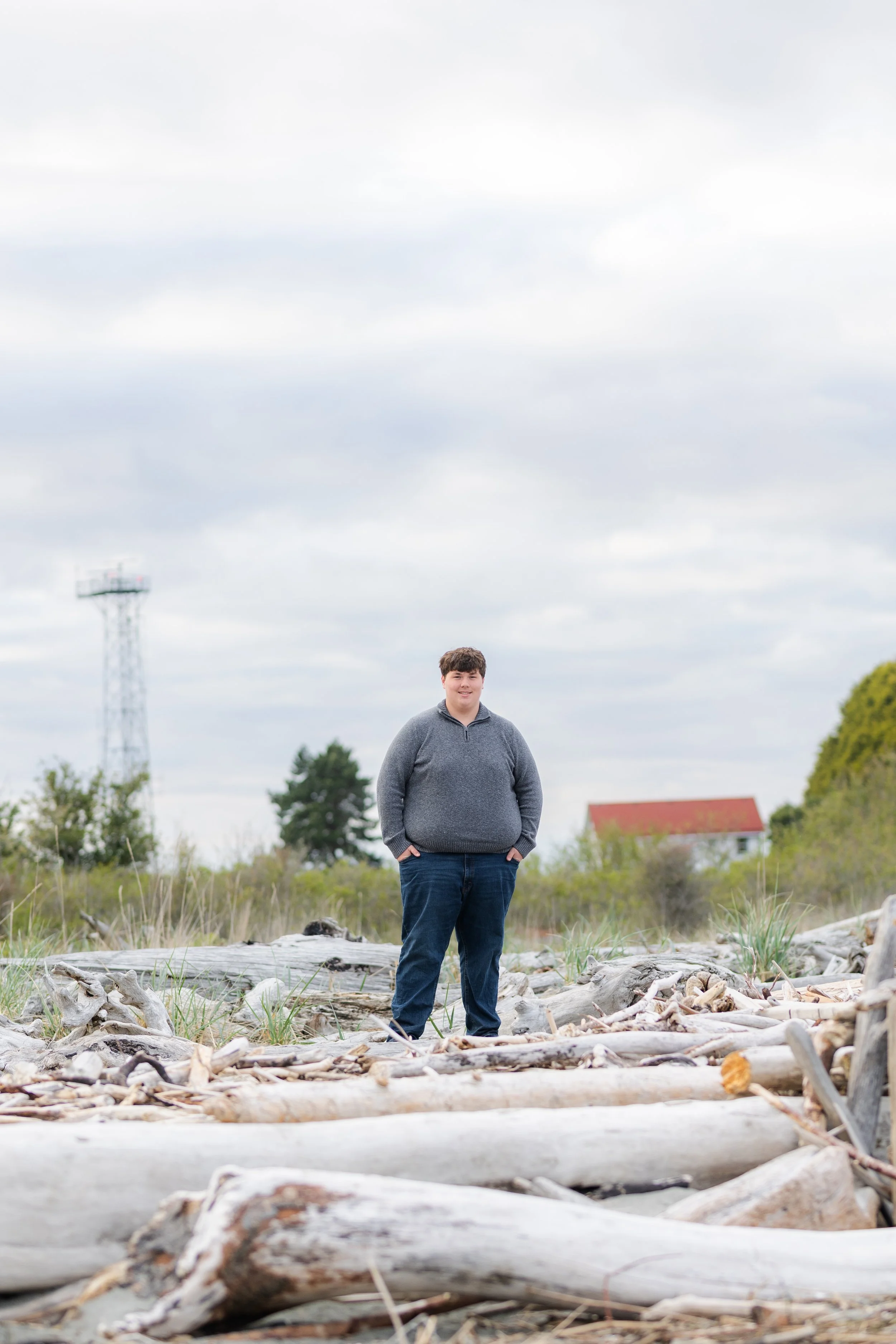 Senior picture of a boy standing on driftwood at a beach in North Kitsap