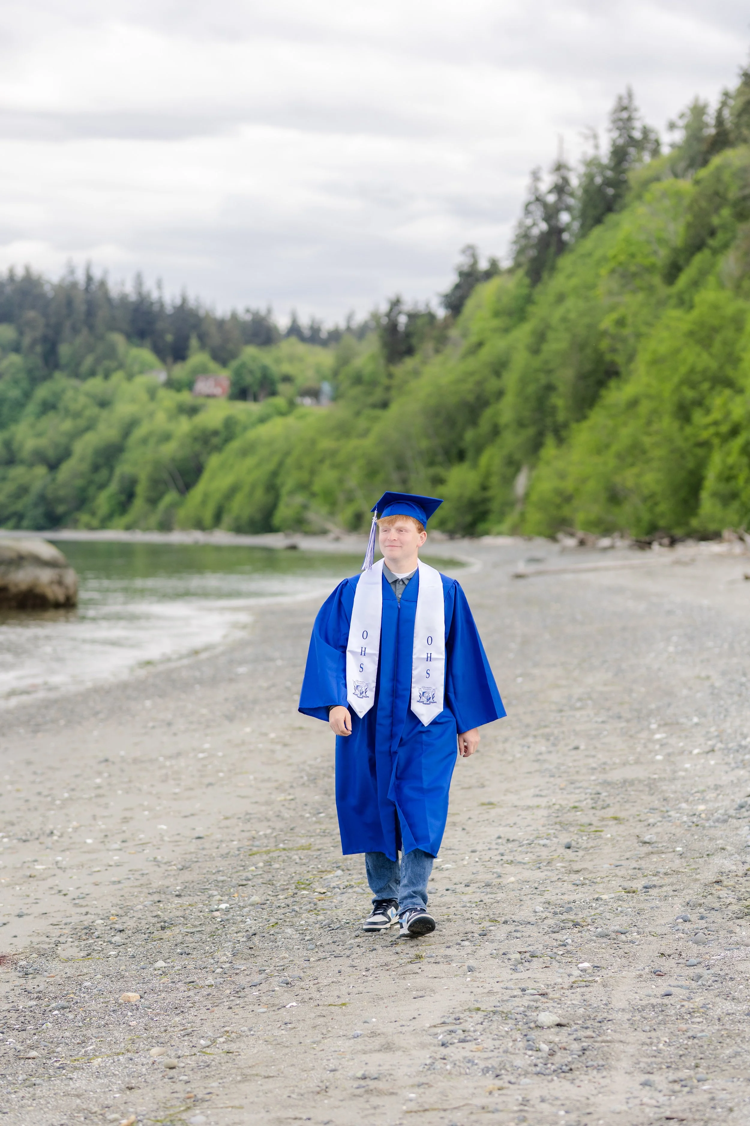 Olympic High School graduation picture of a senior boy walking on the beach in cap and gown