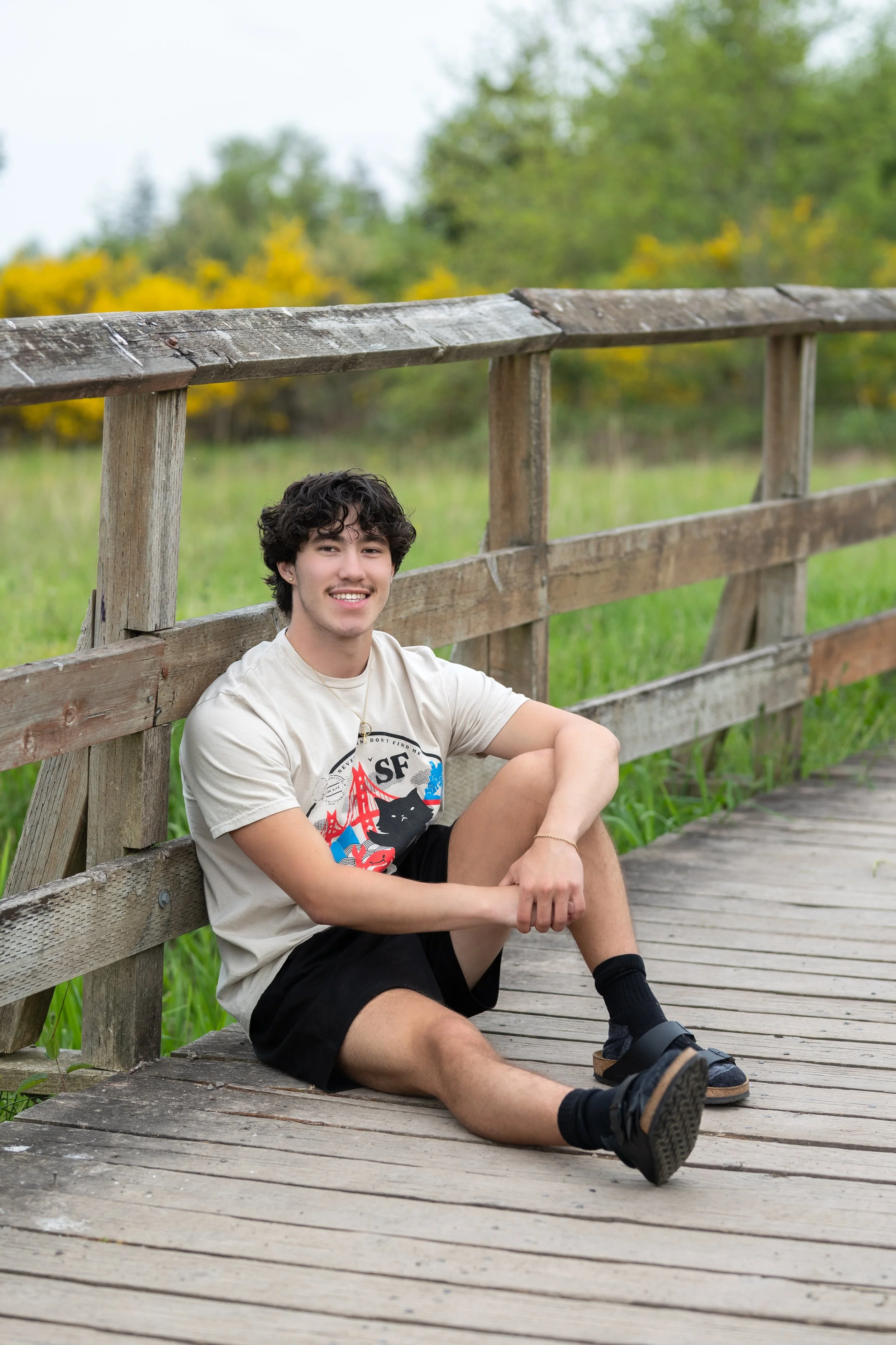 Senior photo of a boy sitting against a wooden bridge