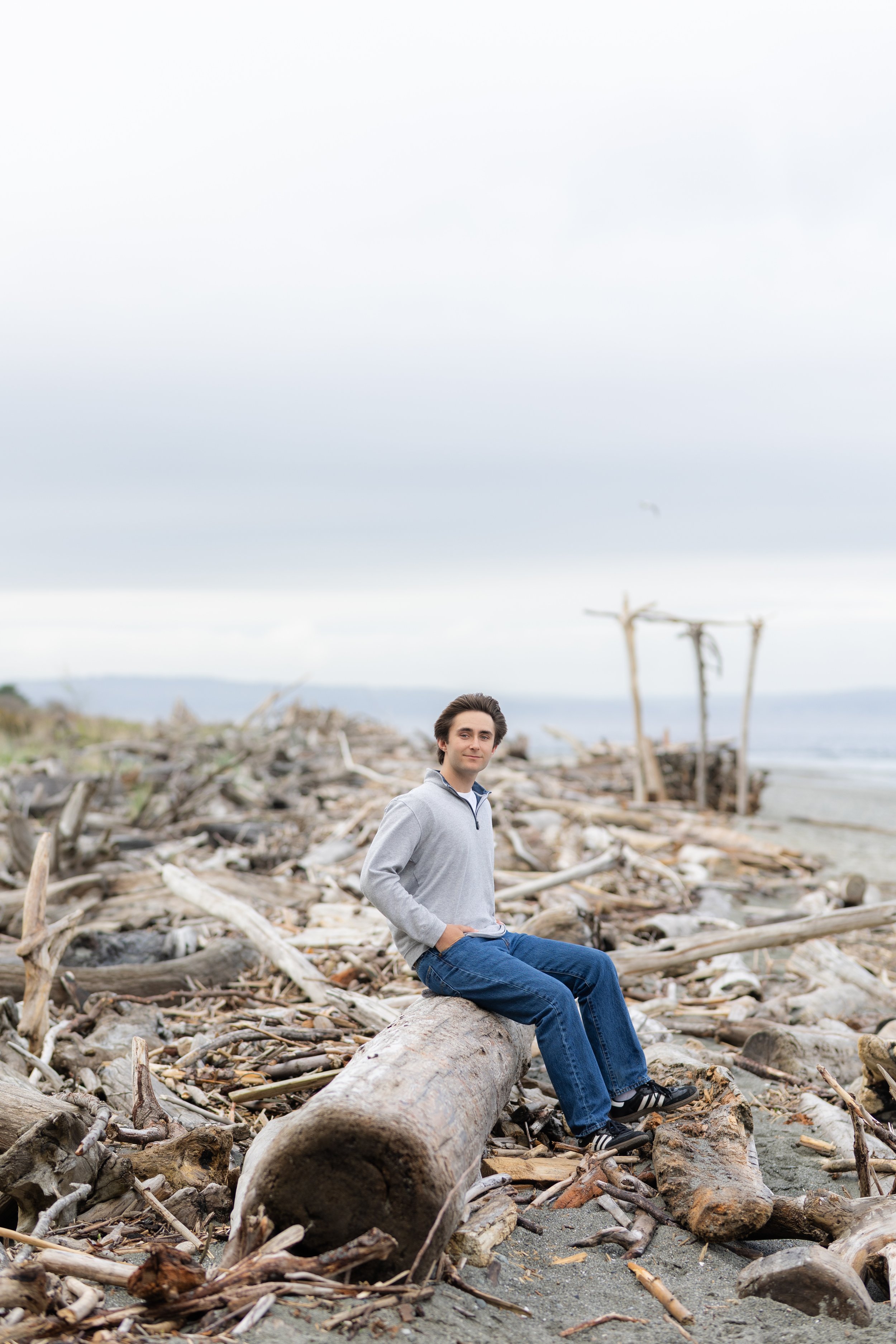 Senior picture of a boy sitting on driftwood at a North Kitsap beach