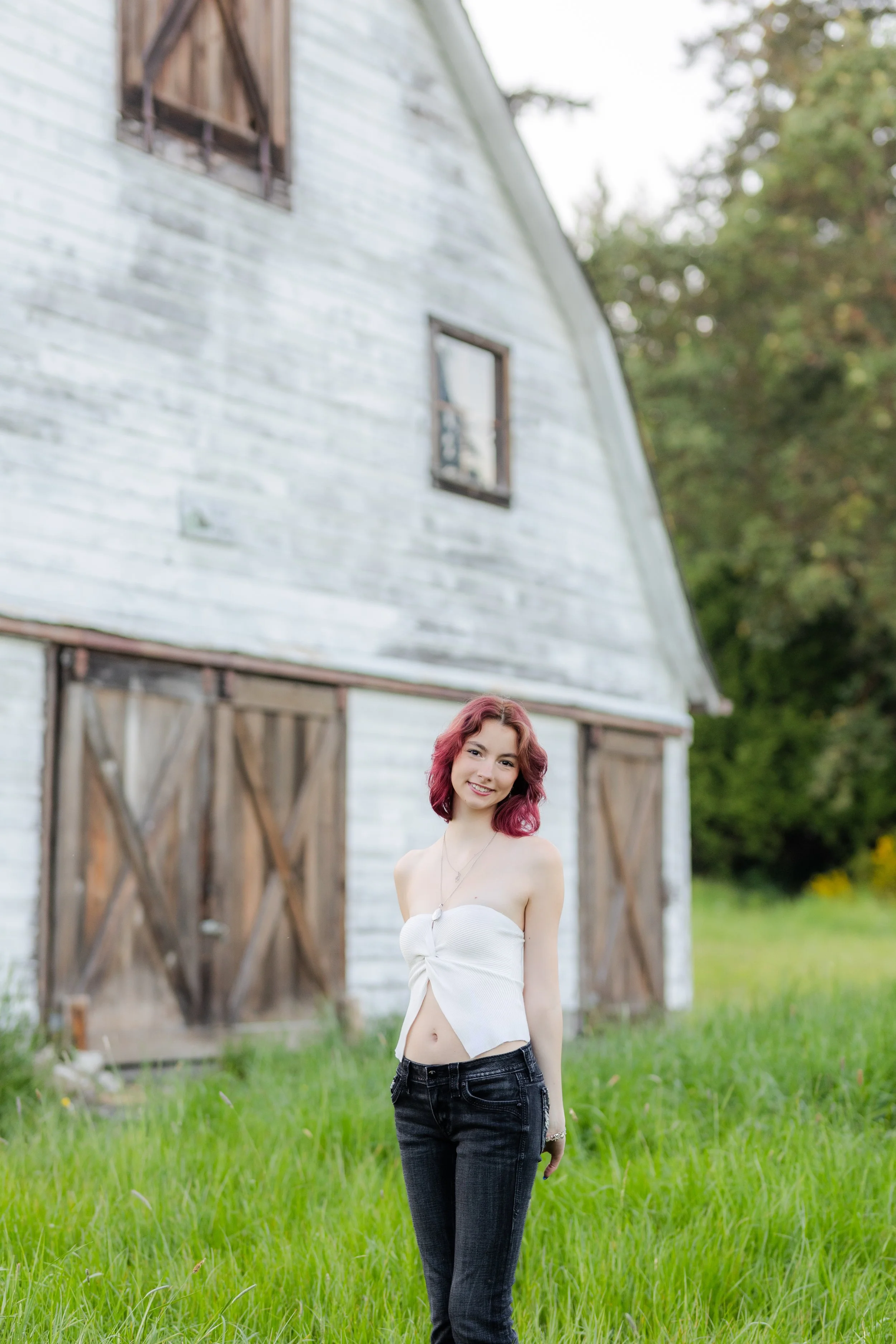 Port Orchard senior picture of a girl with pink hair standing against a white barn