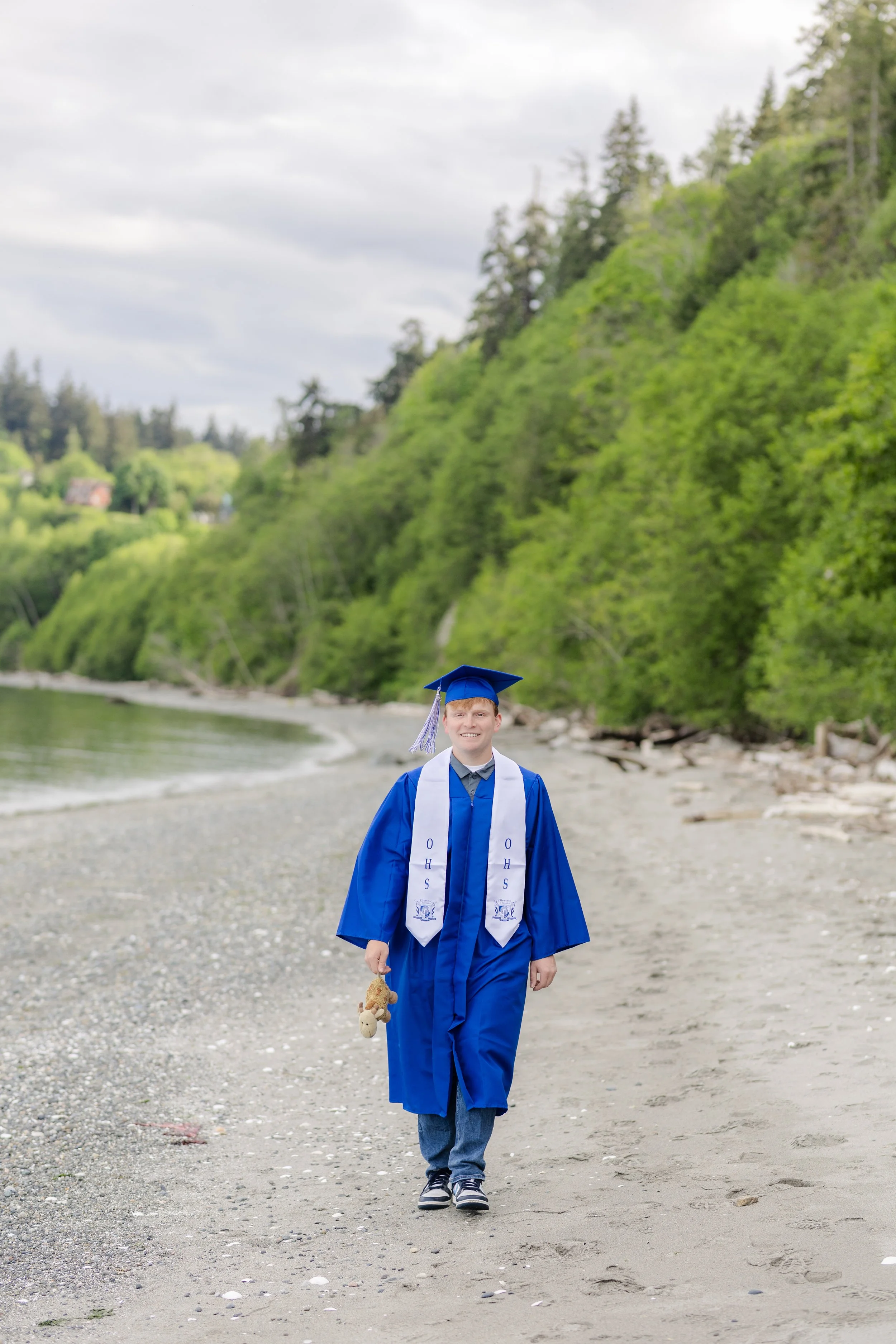 High school graduate walking with childhood stuffed toy at a beach in Washington state