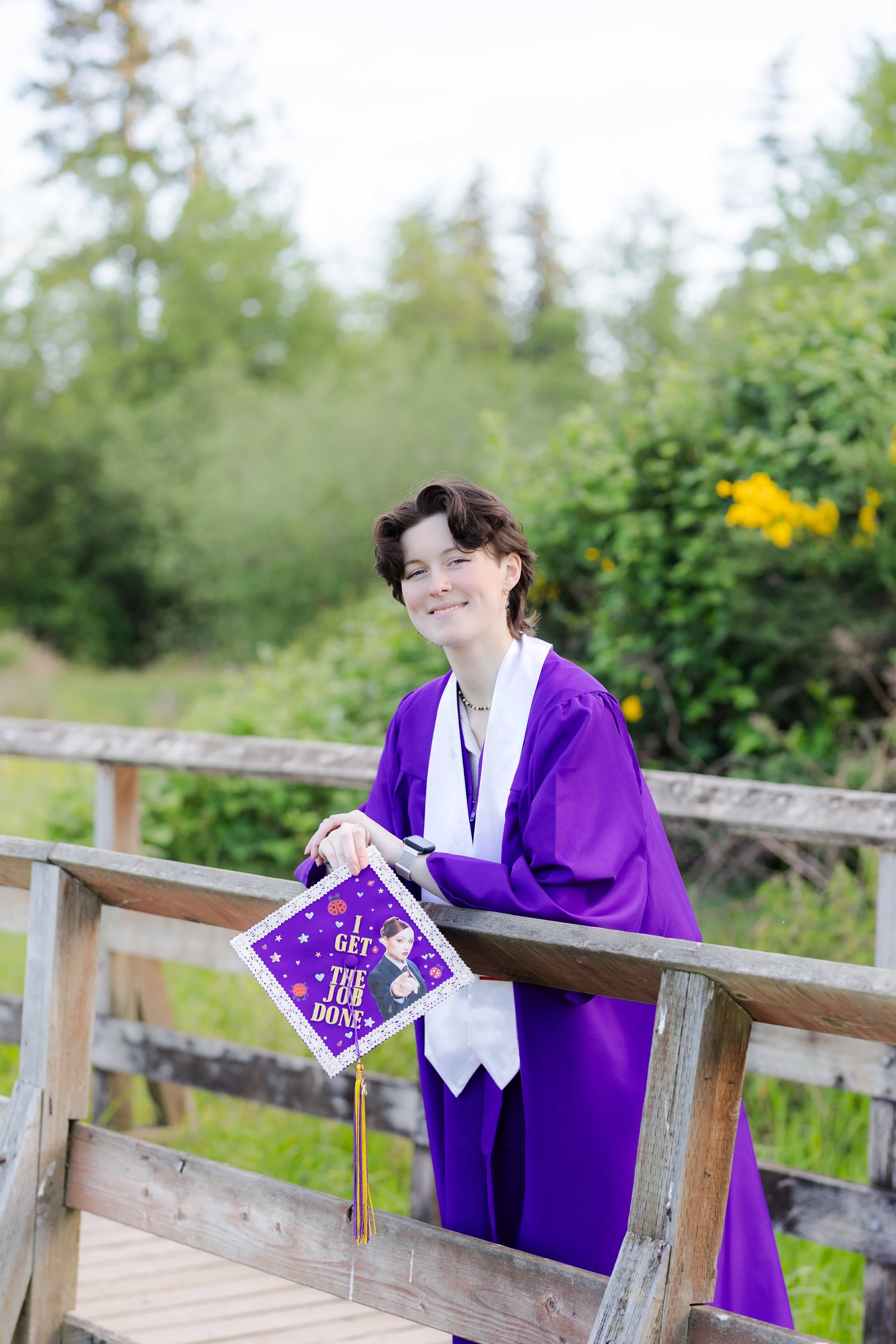 Kitsap cap and gown picture of a grad leaning against a wooden bridge