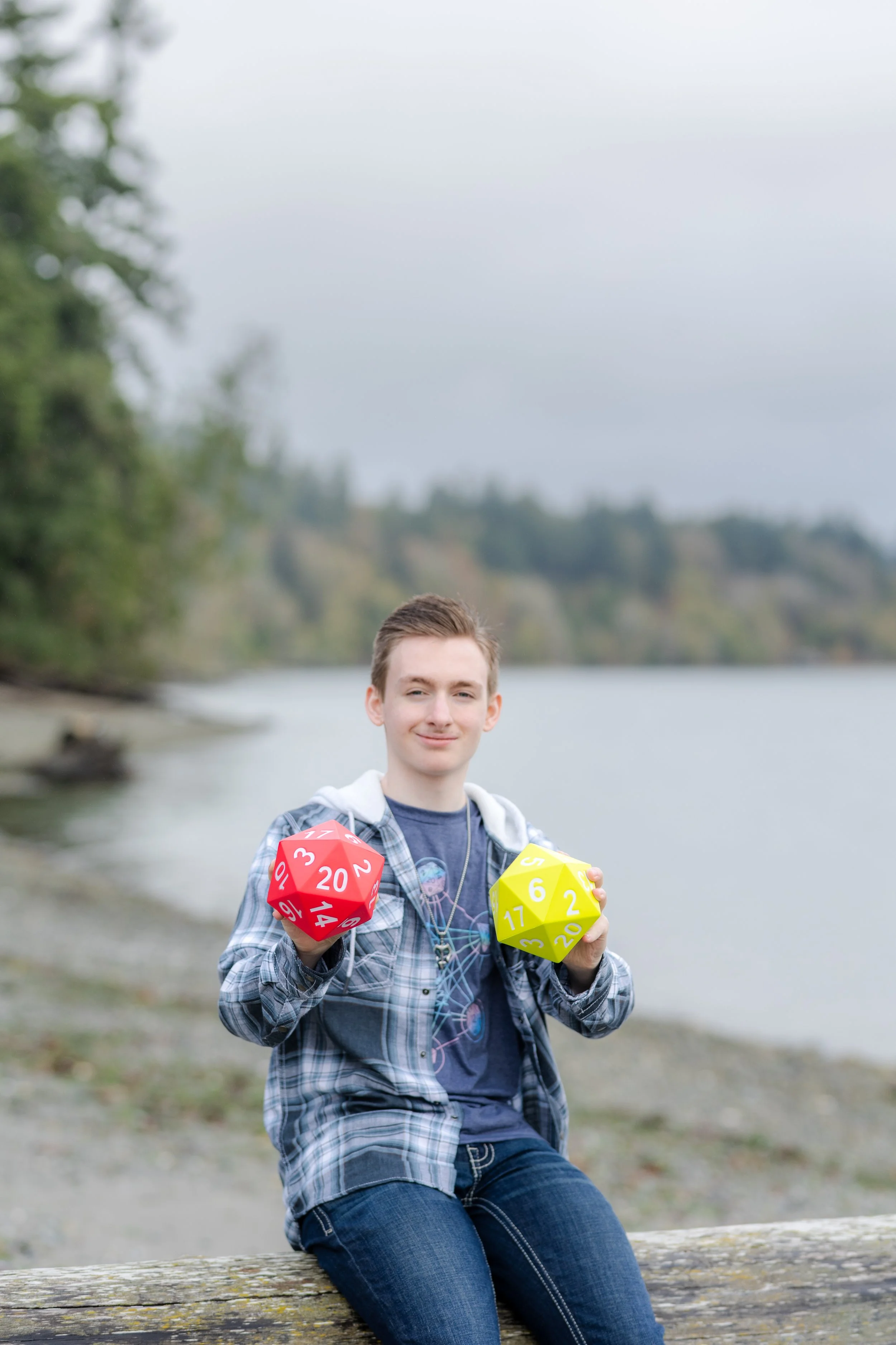 Senior picture of boy on Washington beach holding dice from the game "Dungeons and Dragons" with the numbers 20 and 6 showing, indicative of his graduation year, 2026.