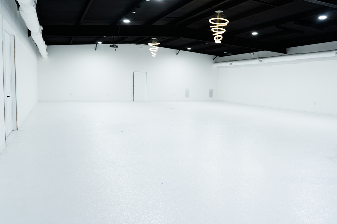 Empty white room with black ceiling, modern spiral hanging lights, and minimal decor.
