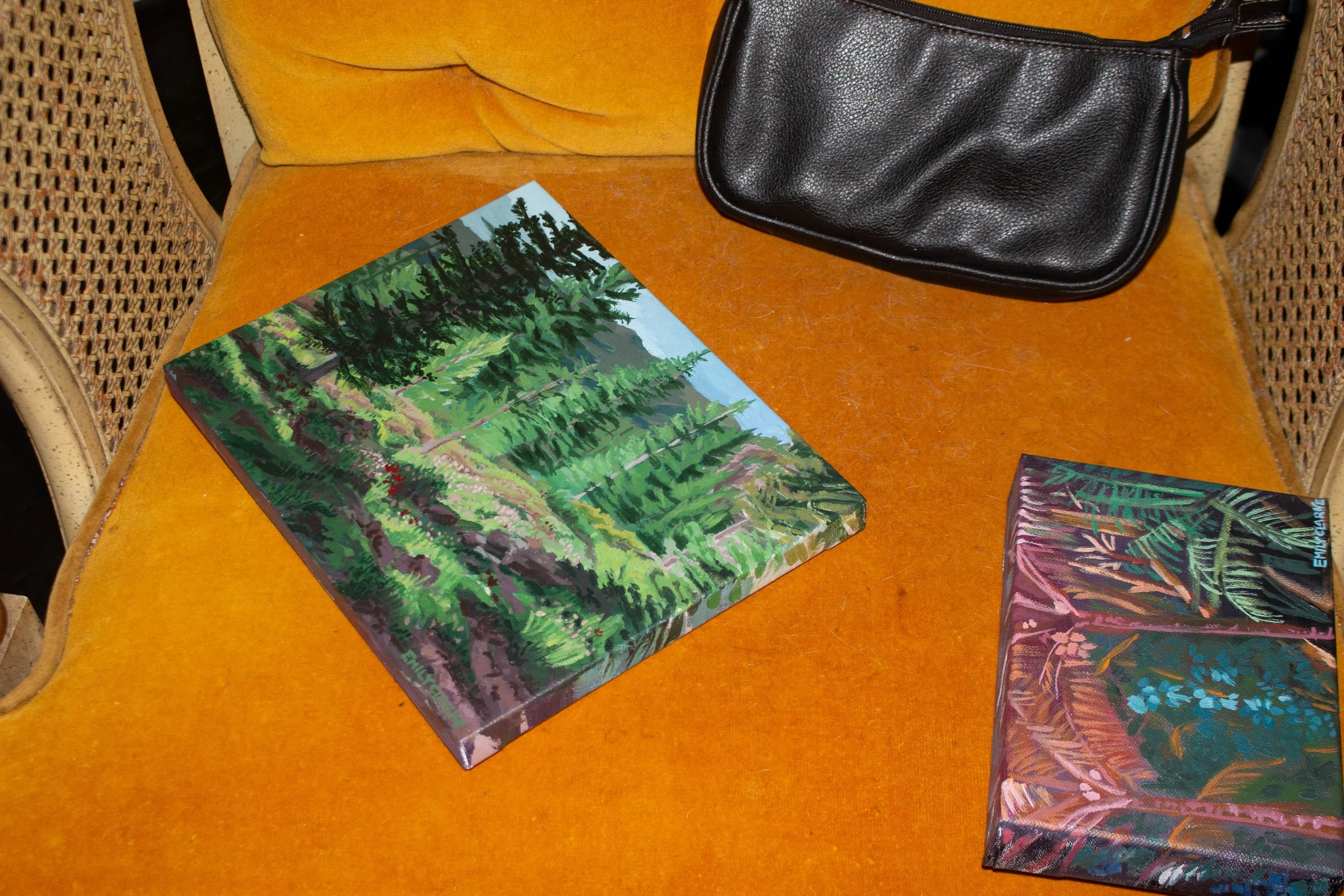 Colorful paintings of nature and a black clutch bag on an orange chair.