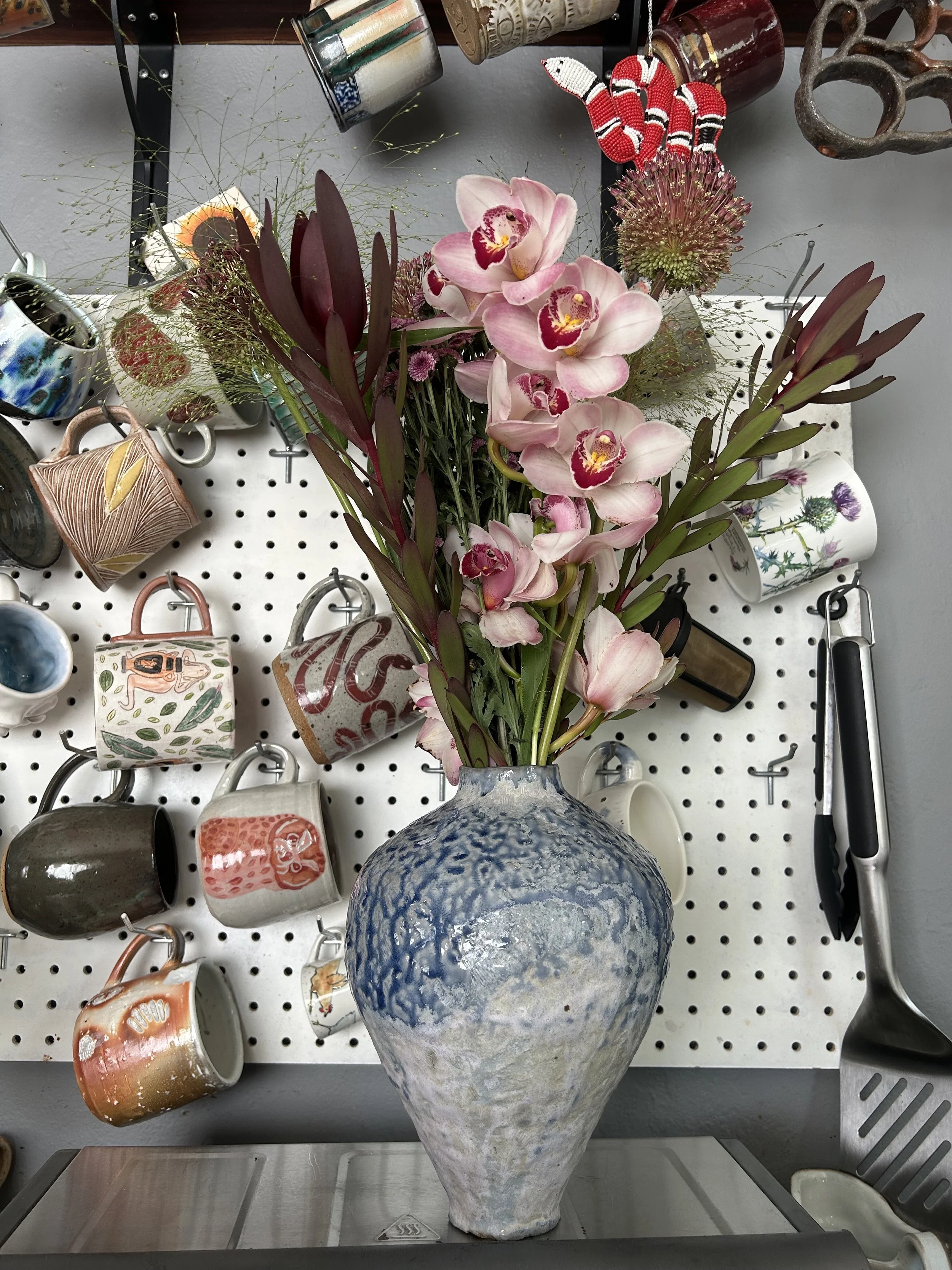 Soda Fired Vase with Flowers and a Mug Wall Behind