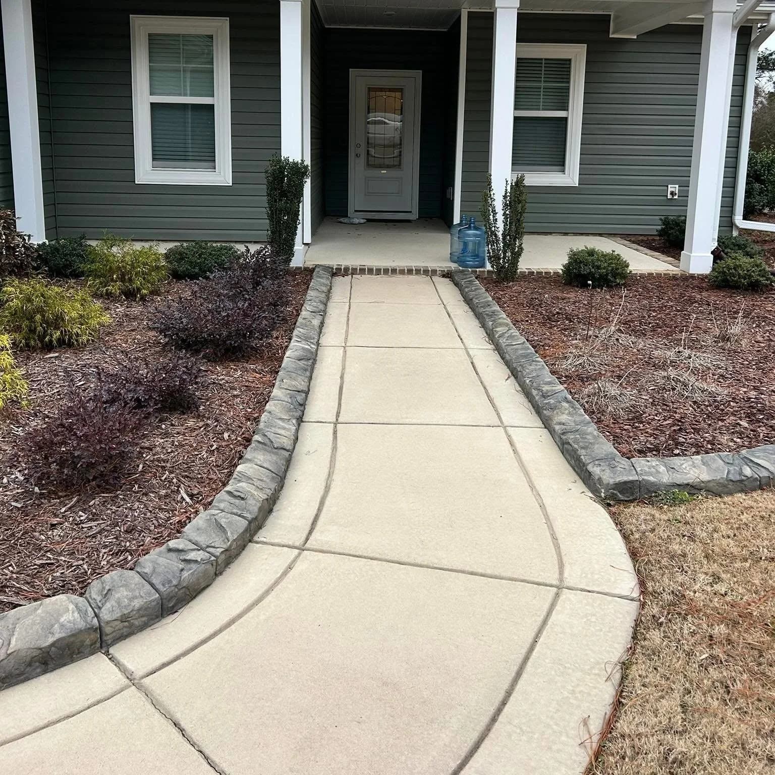 FFront of house with walkway and garden beds edged with curved concrete curbing with a stone look