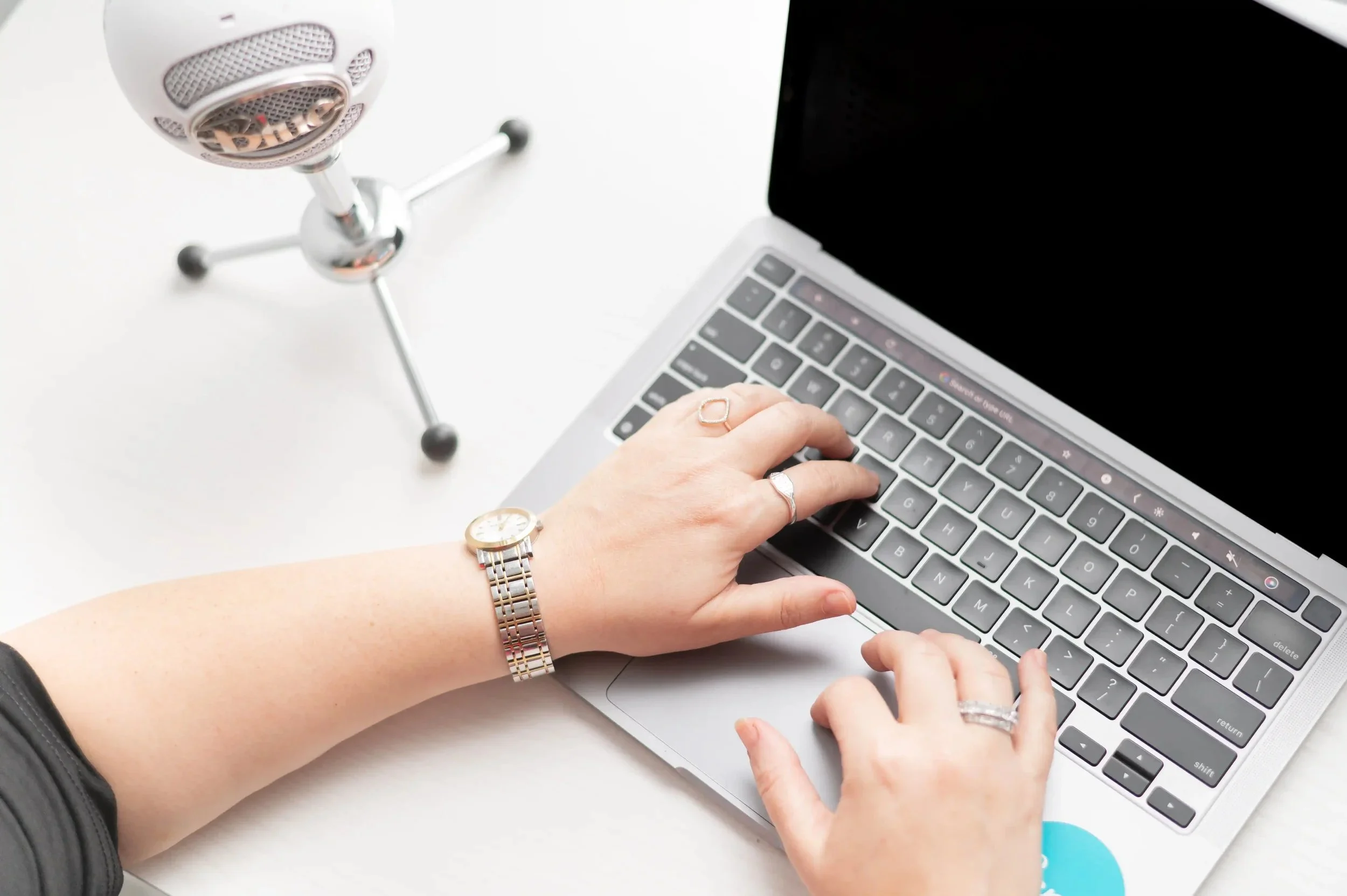 Person typing on a silver laptop with a microphone on a stand nearby.