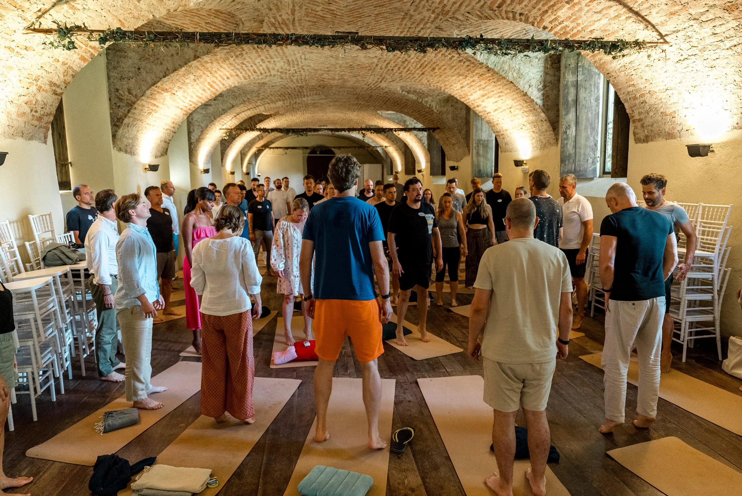 Menschen nehmen an einem Yoga- oder Meditationskurs in einem Raum mit hohen, gewölbten Backsteindecken teil.