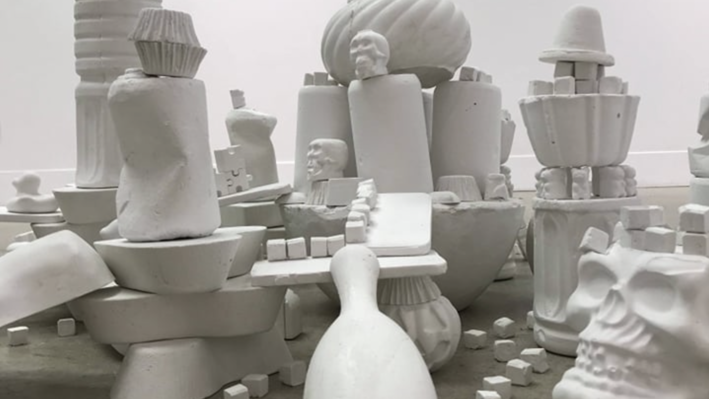 A collection of white ceramic sculptures and objects, including skulls, heads, vessels, and abstract forms arranged on the floor.