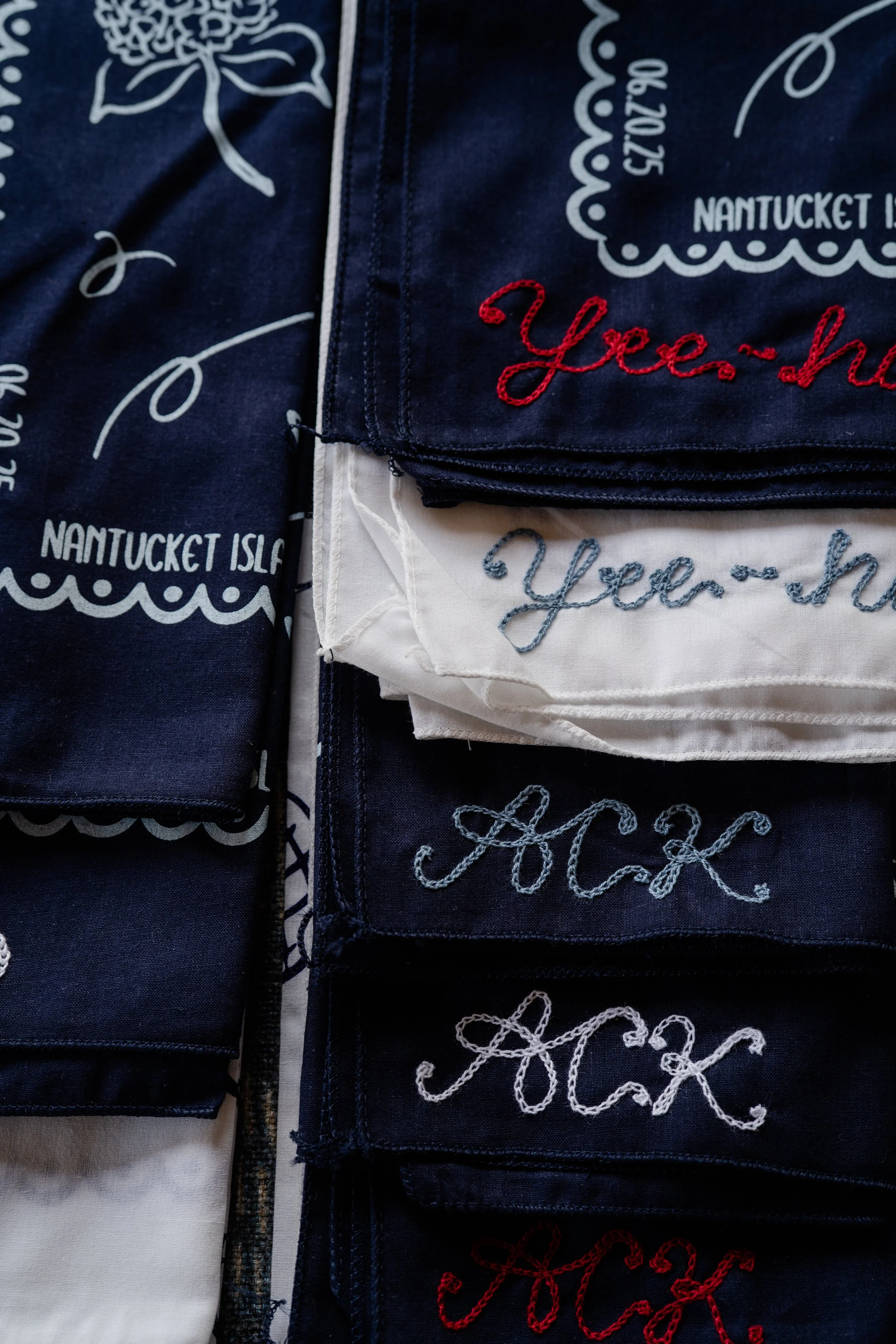 Custom chainstitch bandanas are lined up for wedding guests. The bandanas are navy blue and white with red, white, navy, and marine blue stitching featuring Yee-Haw and  ACK, the Nantucket airport code.