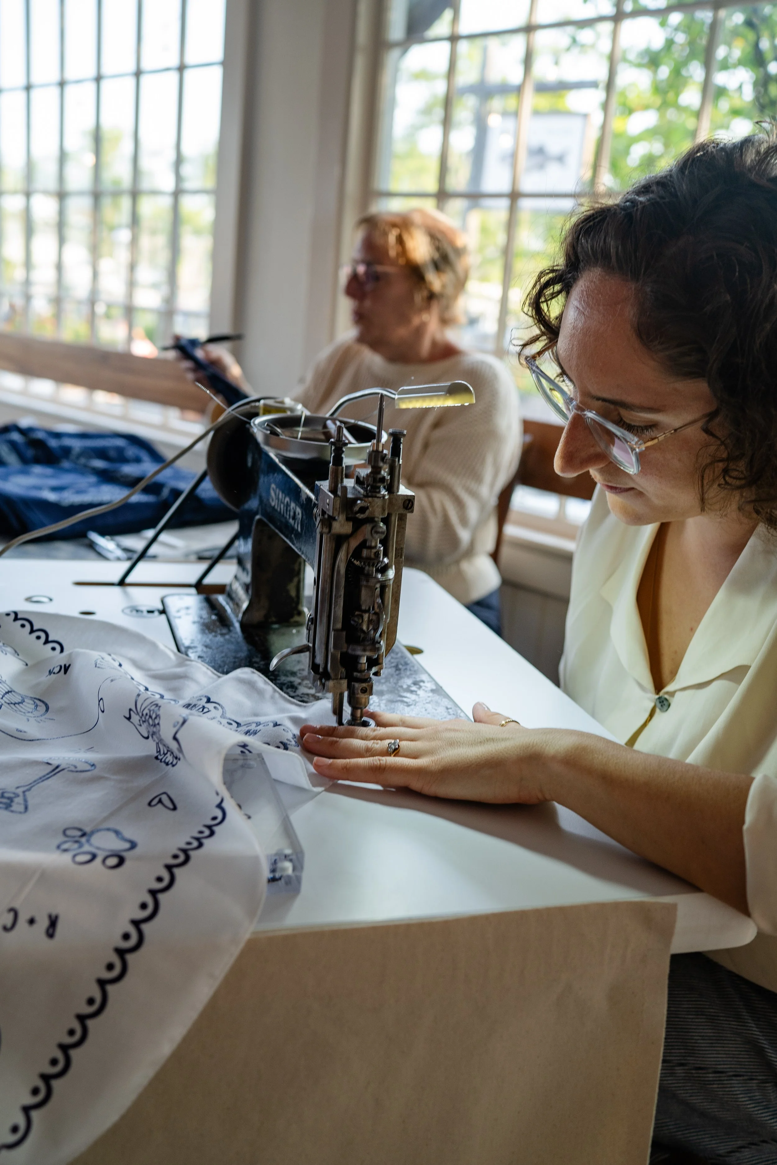 A woman sitting behind a chainstitch embroidery machine, embroidering a bandana at a wedding.