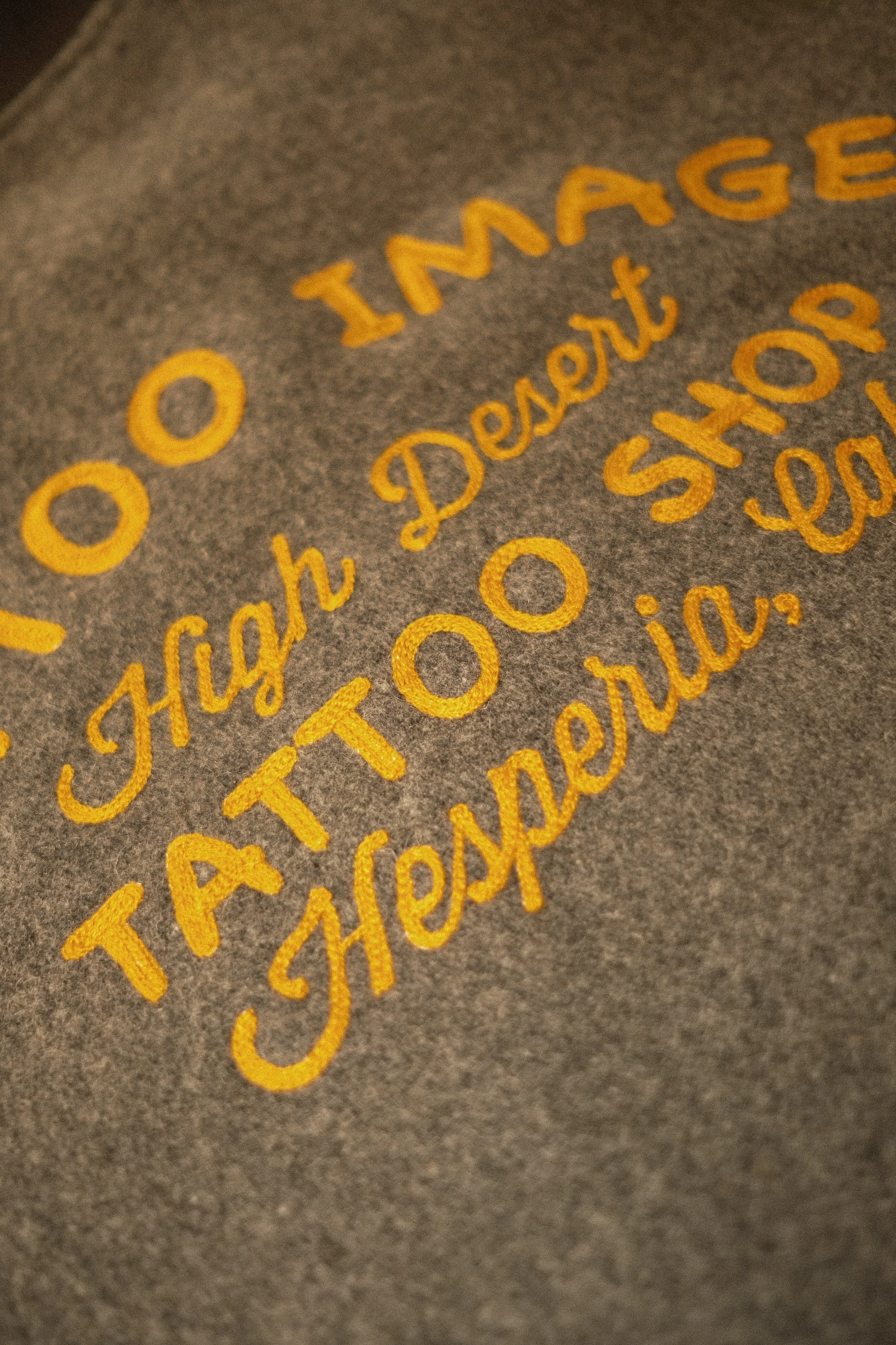 Golden yellow chainstitch embroidery on the back of a gray wool clicker coat for a local tattoo shop in Hesperia, California