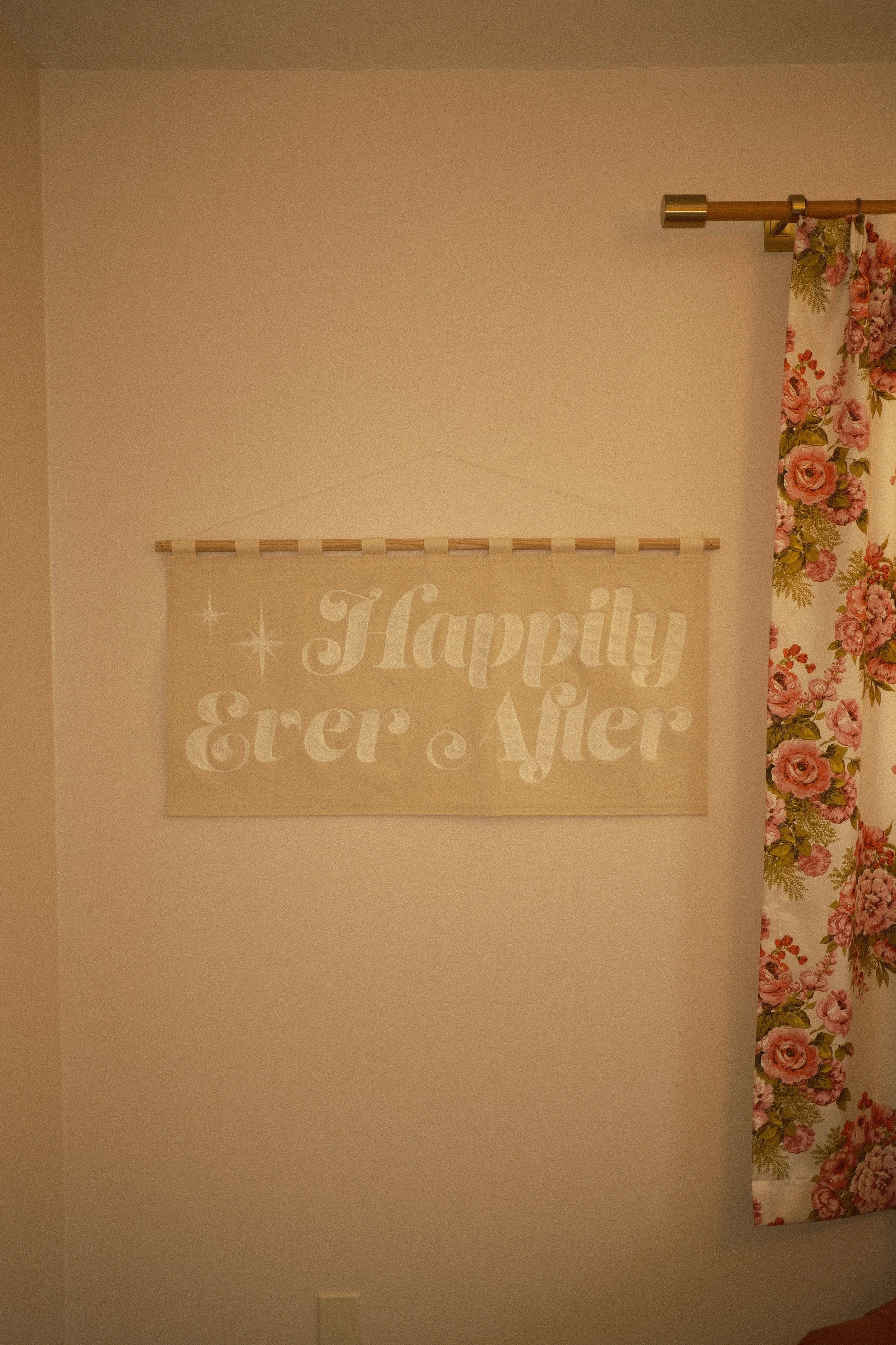 A cream colored canvas banner reading "Happily Ever After" in white chainstitch embroidery