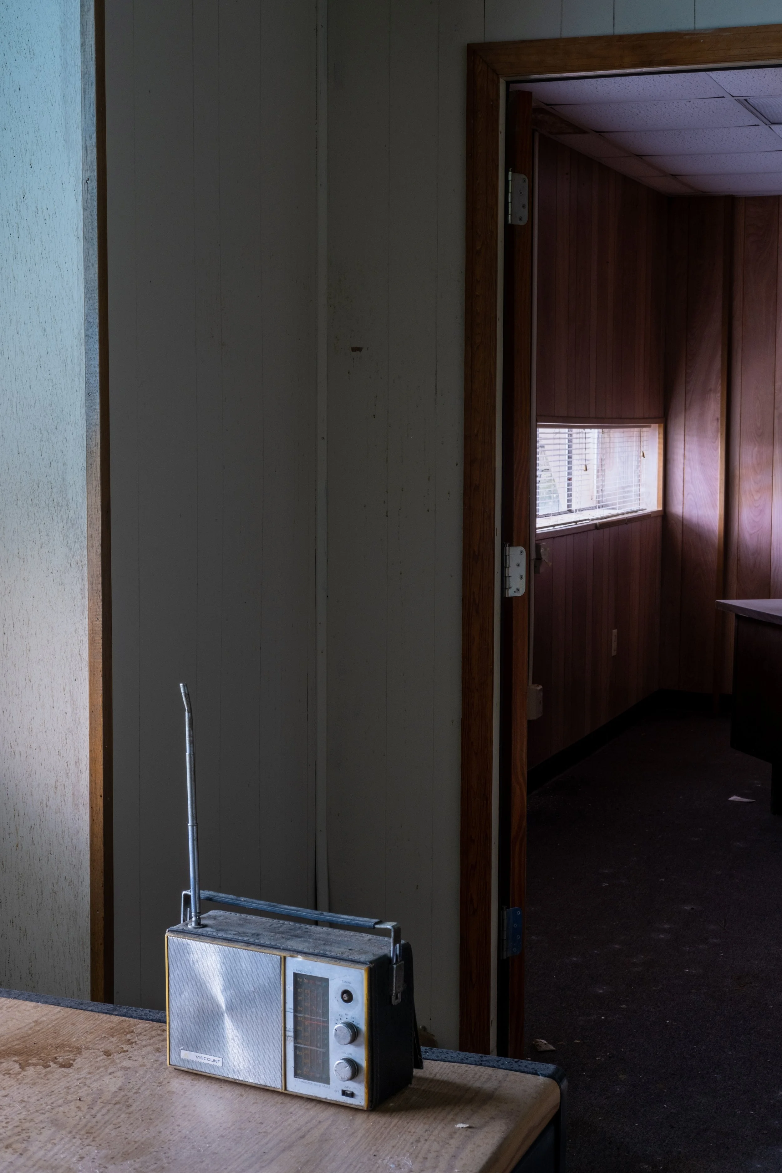 An old portable radio sitting on a wooden surface inside an abandoned building.
