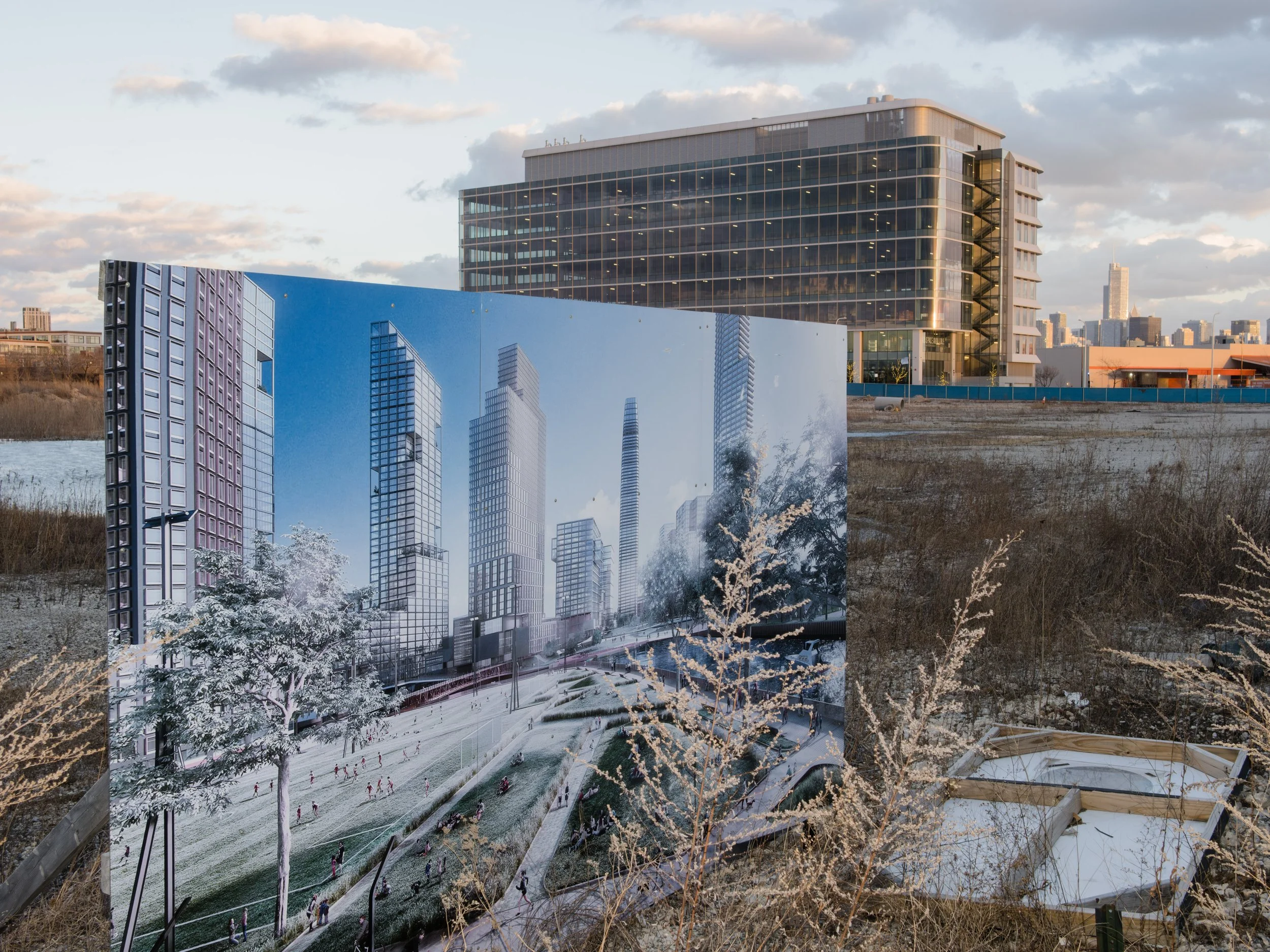 A large outdoor billboard displays a digital rendering of a modern city skyline with tall glass skyscrapers, set against a partly cloudy sky. The billboard is situated in an open, grassy area with sparse vegetation, and a commercial building is visib
