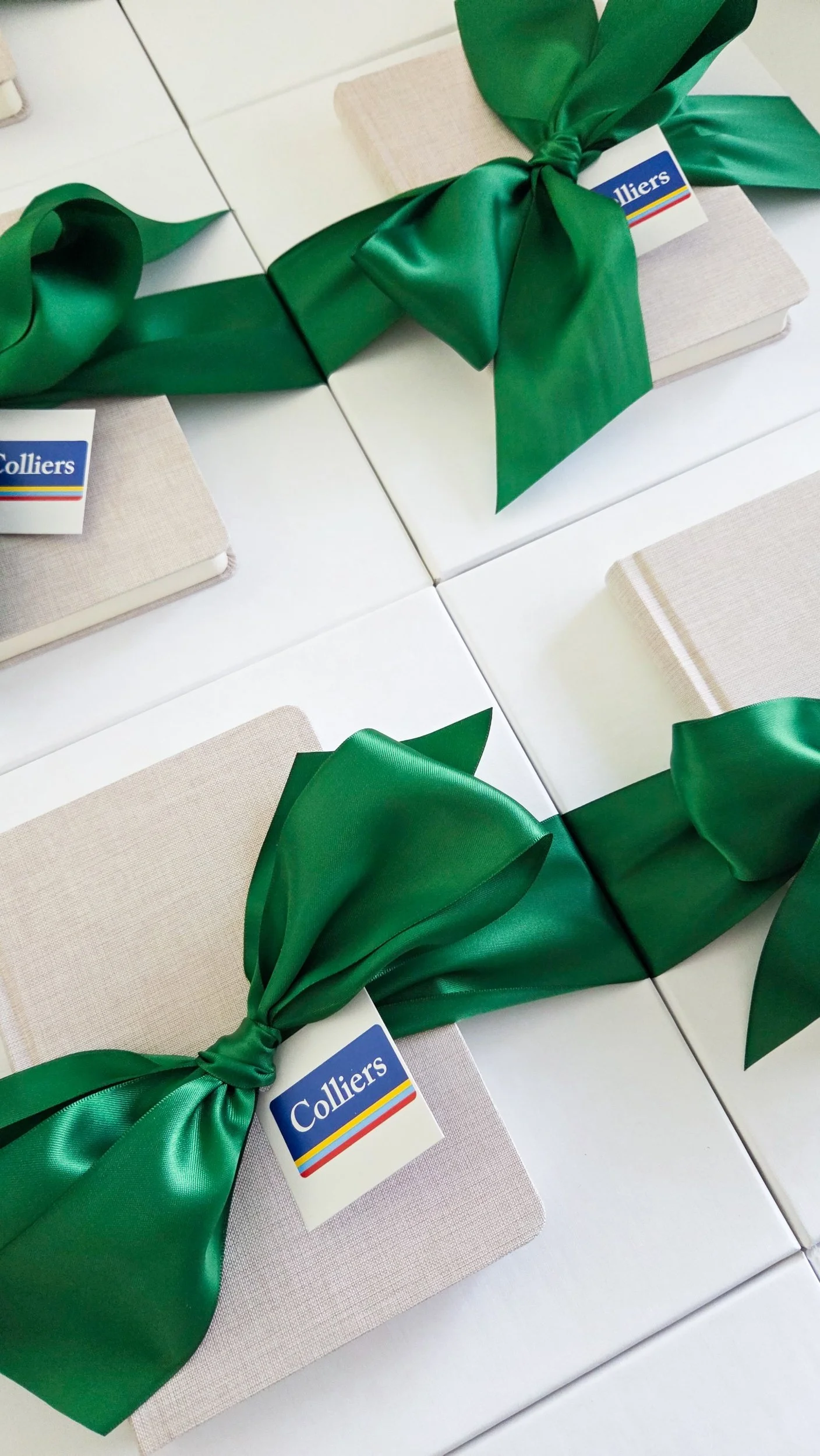 Closed beige gift boxes wrapped with large green satin bows and tags labeled 'Colliers'.