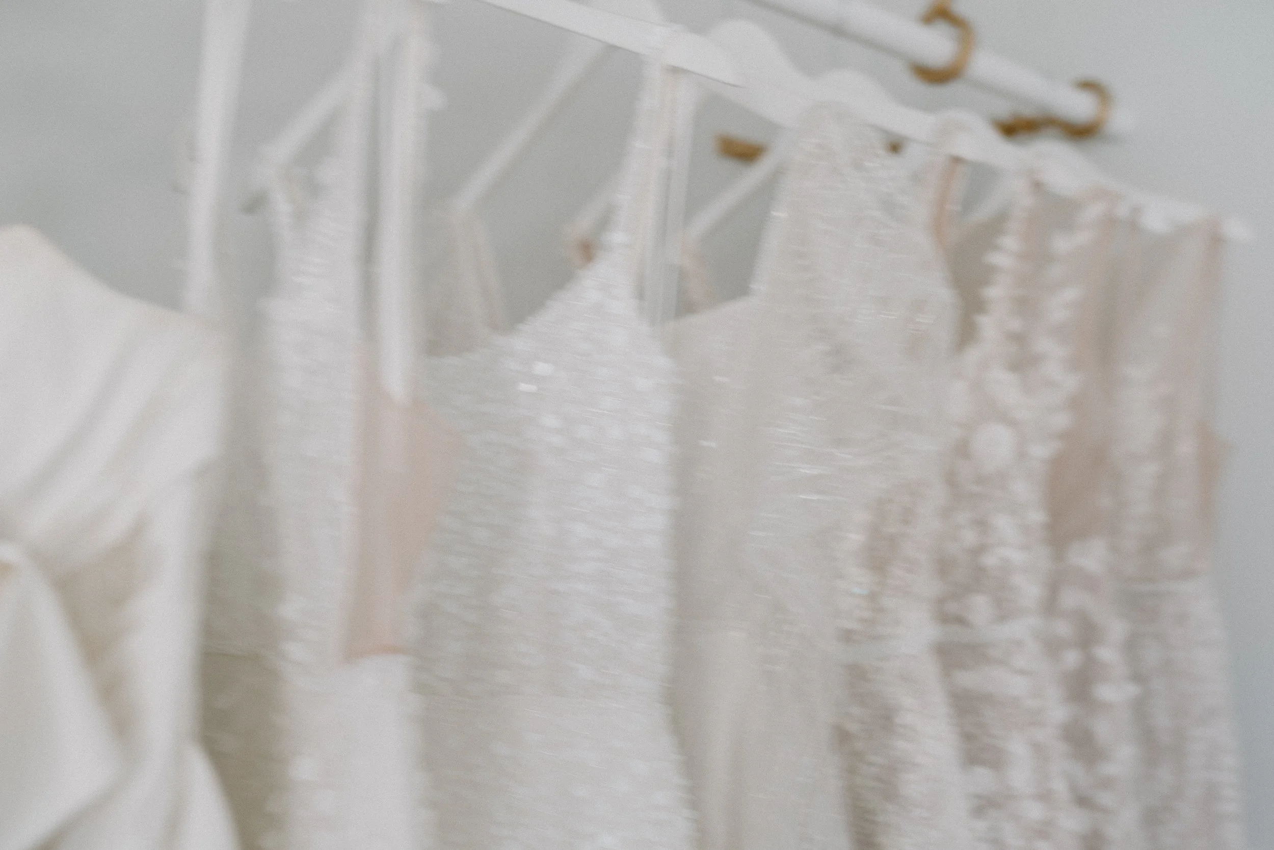 A row of white wedding dresses hanging on golden hangers on a white closet rod.