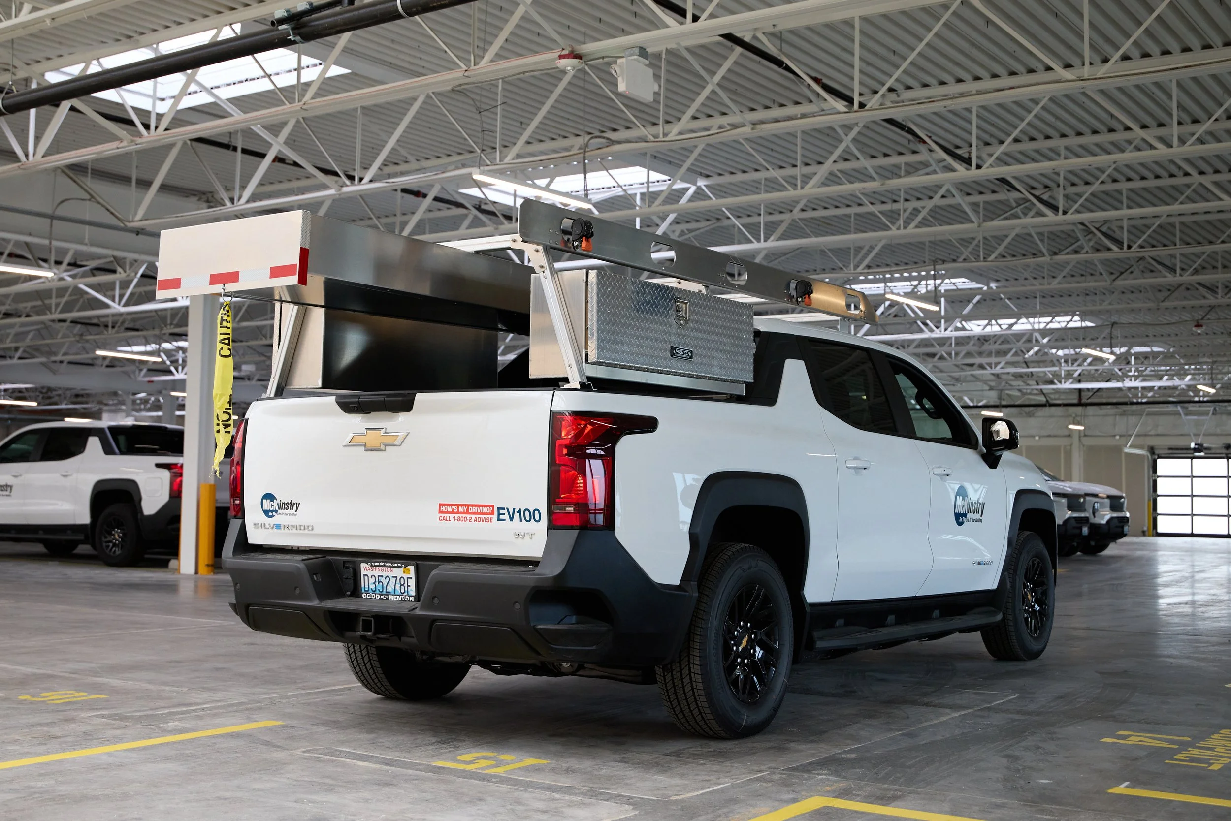 The back of a white pick up truck. Inside the truck bed is silver work equipment.