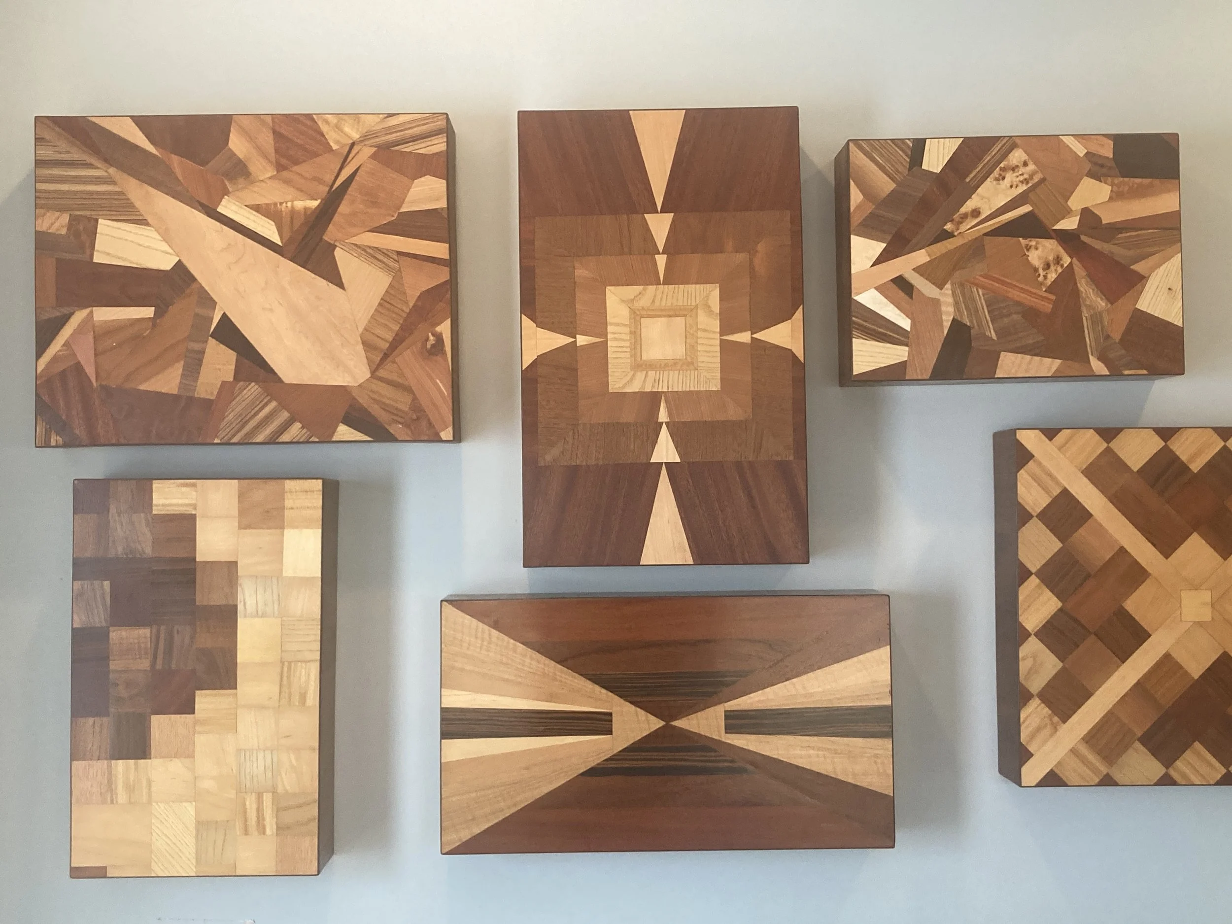 Collection of six geometric wooden puzzle boxes with various patterns mounted on a wall.