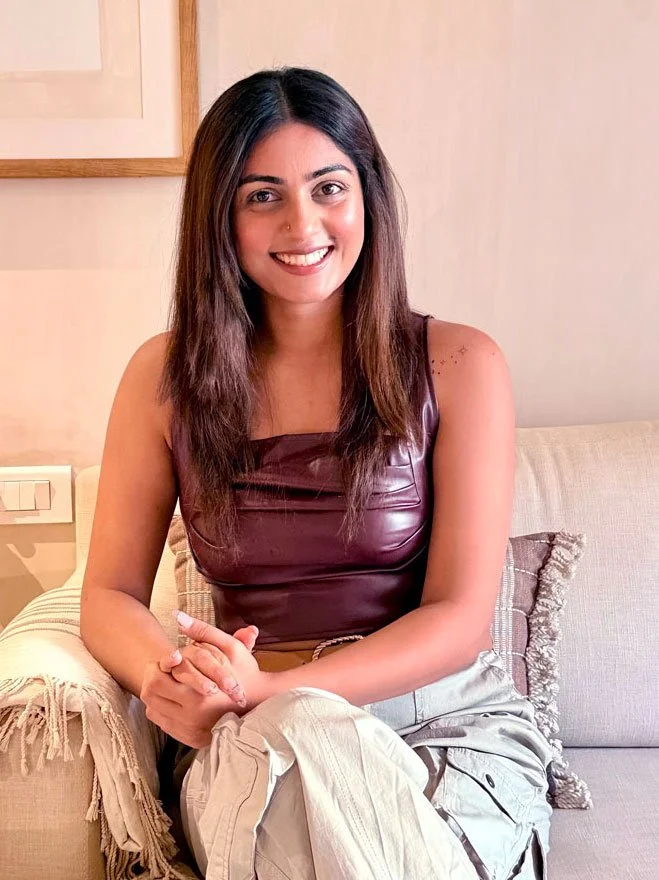 Smiling woman in pink traditional dress with henna on her hands, wearing pink earrings, at a decorated outdoor setting, possibly a wedding or celebration.