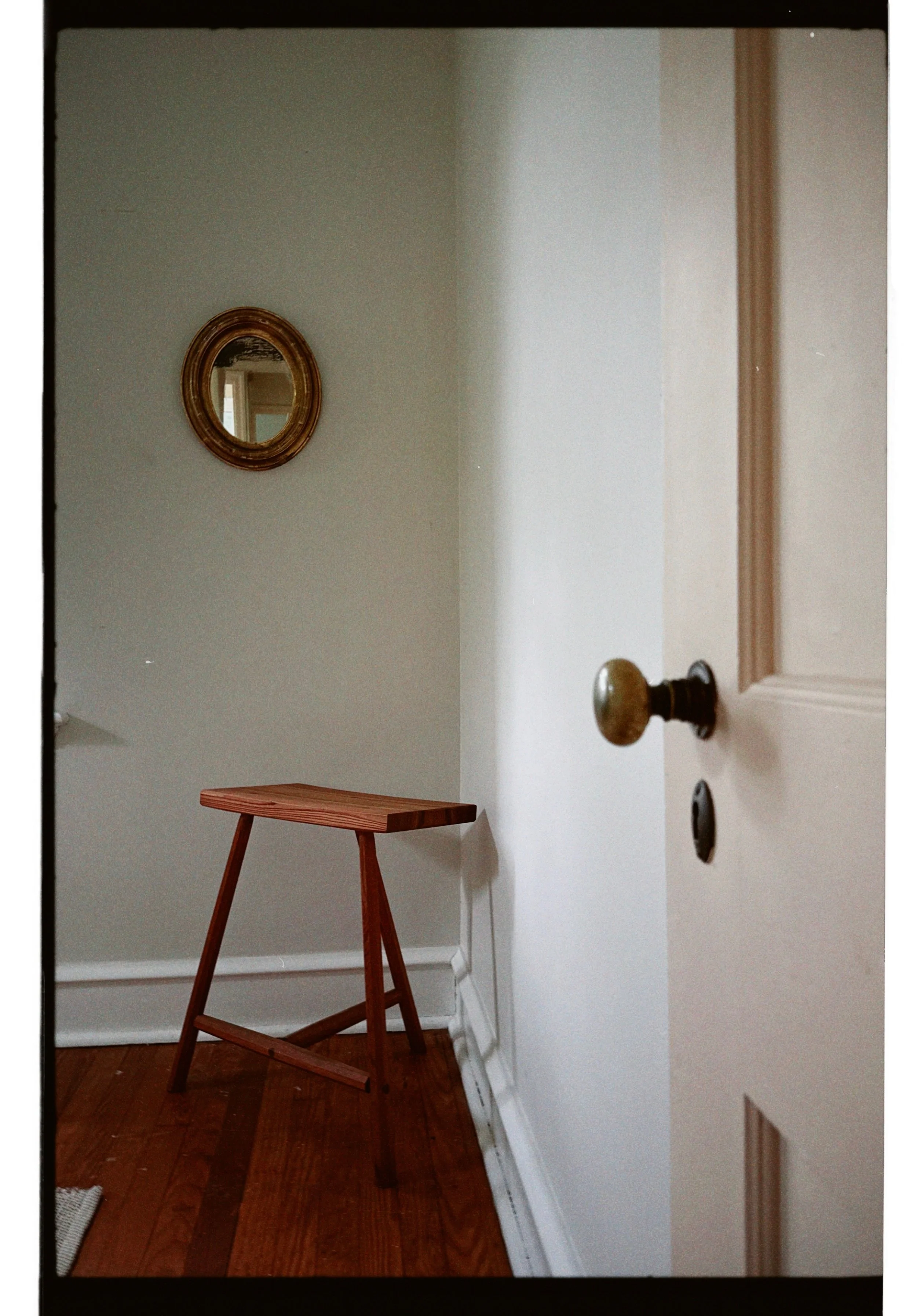 A small wooden table against a beige wall, with a round mirror hanging above. A partially open door with a brass doorknob is visible on the right side.