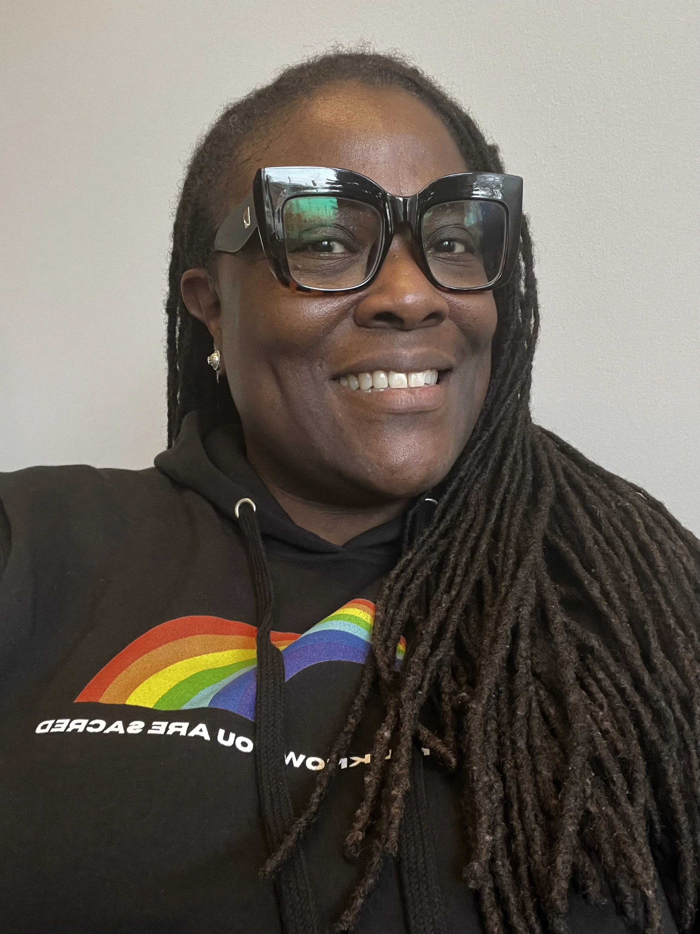 An image of a smiling black woman wearing glasses and a black hoodie