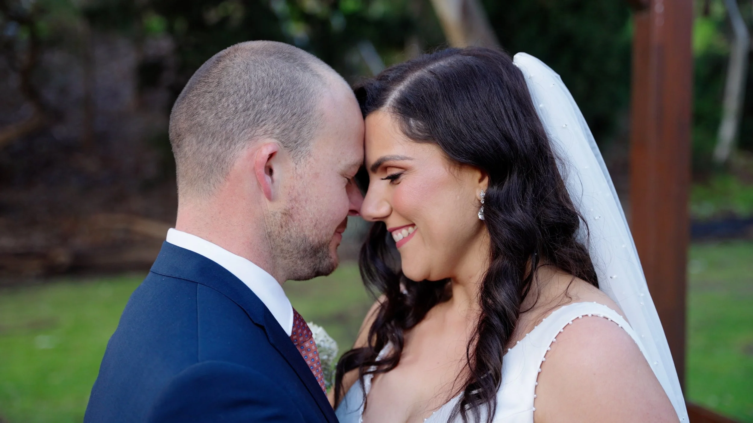 A bride and groom with their foreheads touching during their wedding ceremony outdoors.