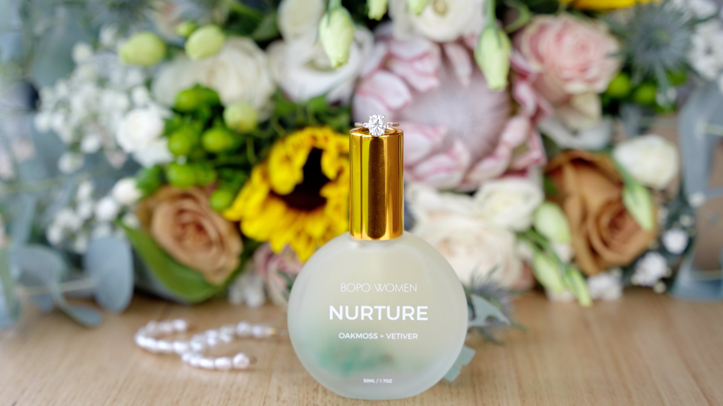 A perfume bottle labeled 'Nurture' by BOPO WOMEN, with a floral bouquet including roses, sunflowers, and greenery in the background.