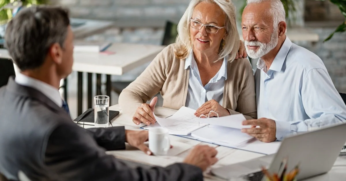 An older couple reviews documents with an estate planning attorney at a table, as they discuss what to put in their trust.