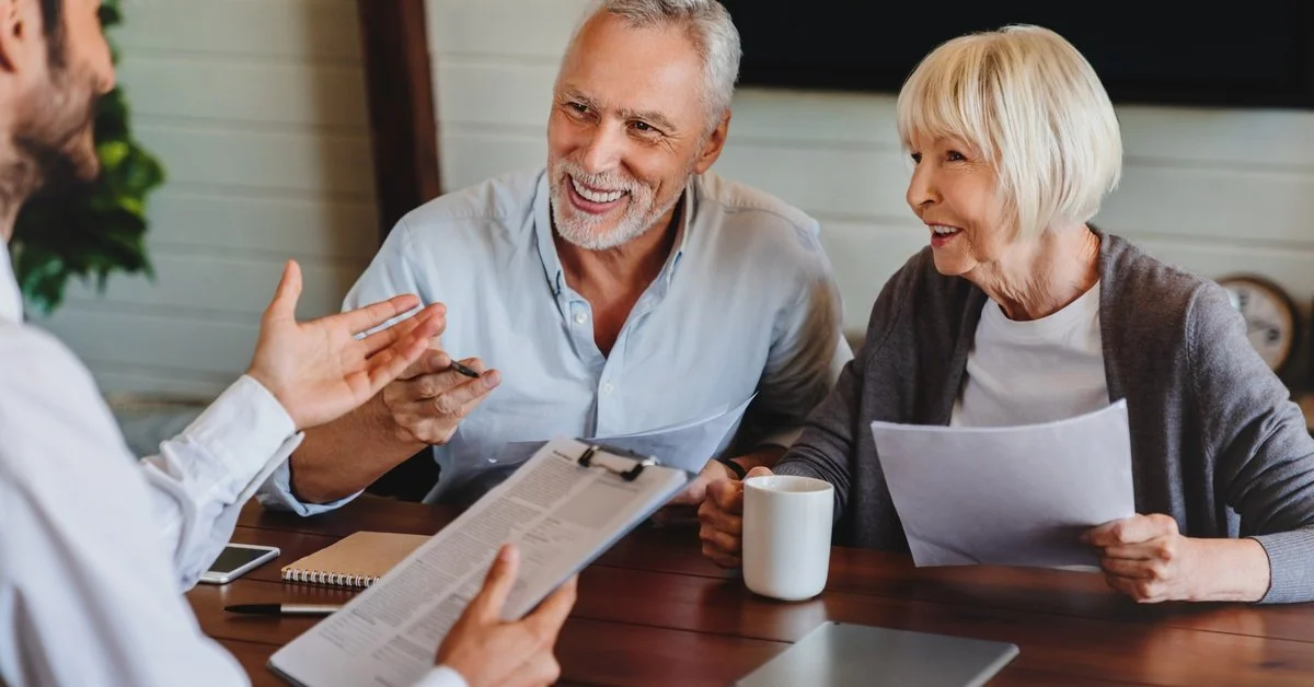 An older couple reviews documents with a lawyer at a table, smiling as they discuss paperwork and estate planning details.