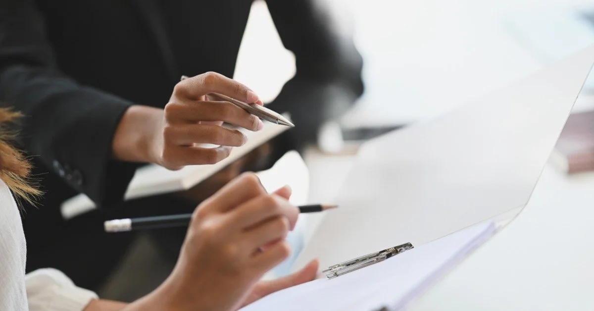 Two women review a document together as one points with a pen and the other follows along with a pencil.