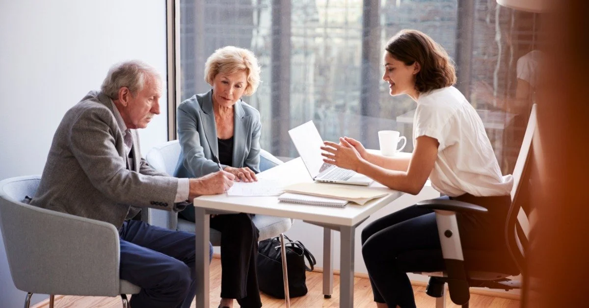 An older couple reviews paperwork with a female lawyer at a desk during a estate planning consultation in an office.
