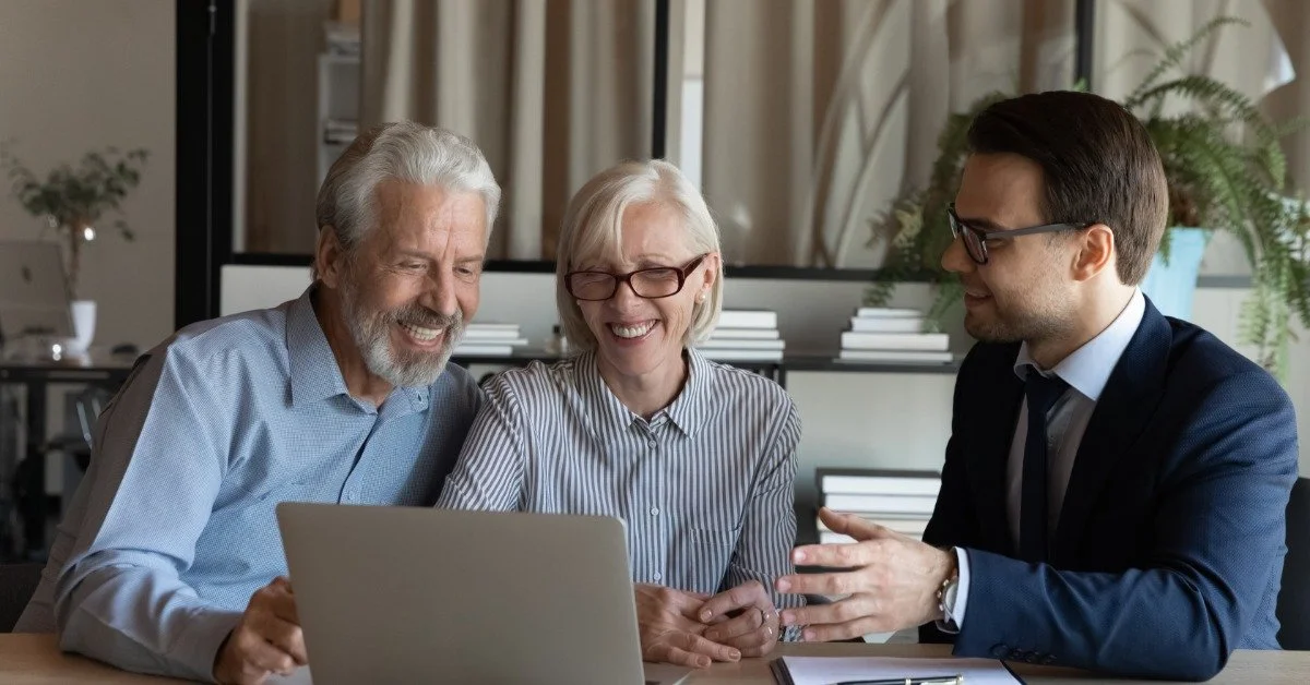 An older couple reviews information on a laptop while a male attorney explains documents across the table.