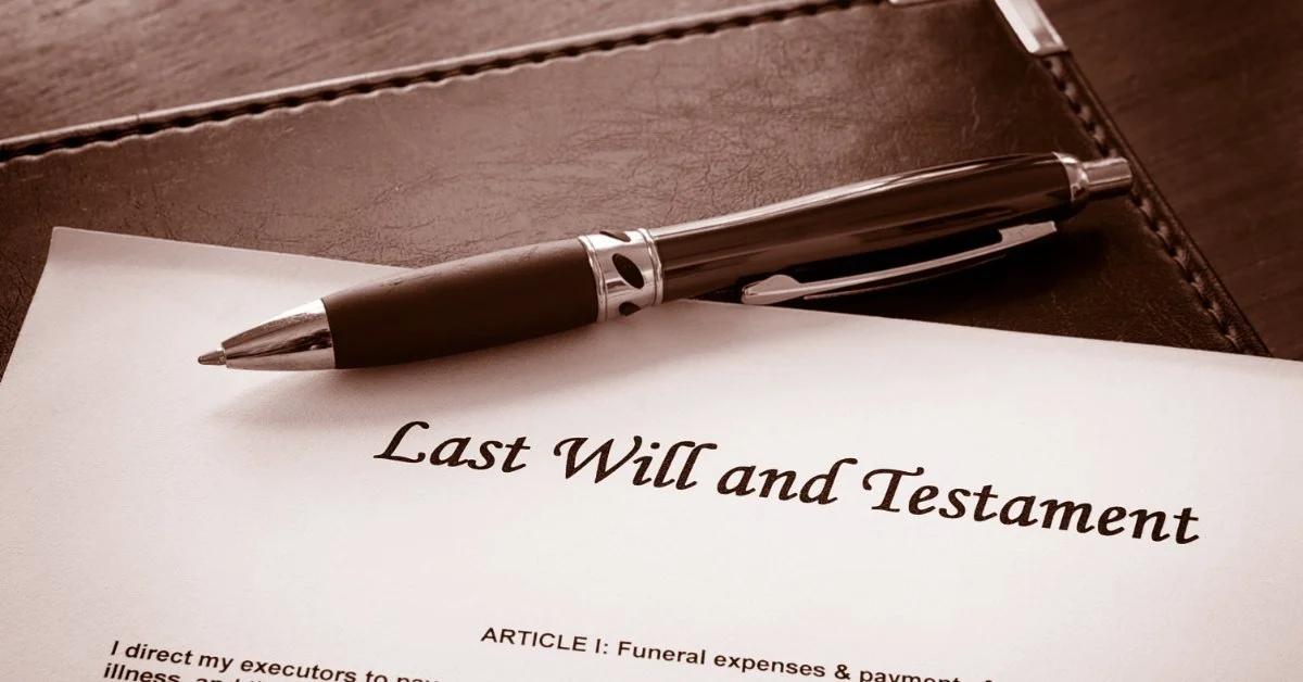 A black pen rests on a last will and testament document beside a leather folder on a dark wooden desk.