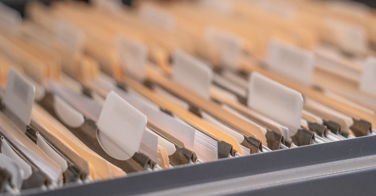 Rows of tan and white hanging file folders fill a metal cabinet drawer, with tabs arranged across the open top.
