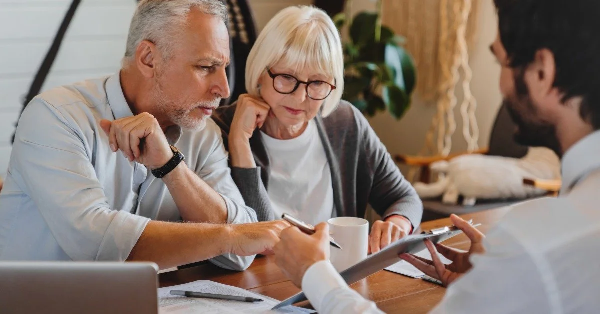 An older couple reviews documents with an estate planning attorney at a wooden table in a bright office.