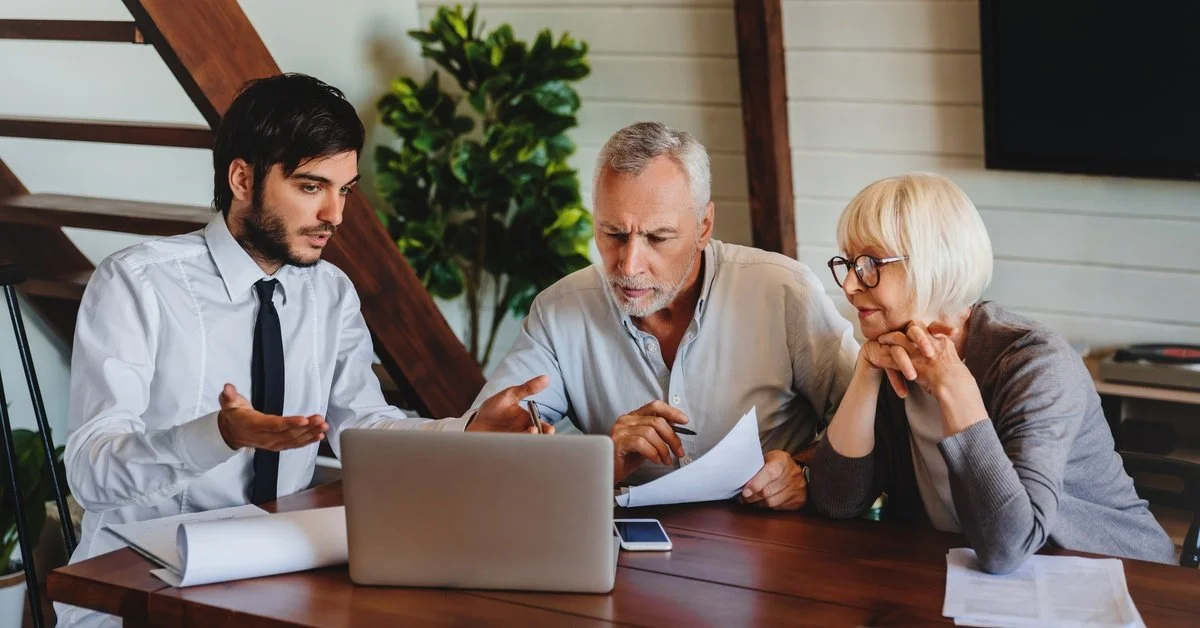 An estate planning lawyer in a white shirt and tie meets with a senior couple reviewing documents at a conference table.