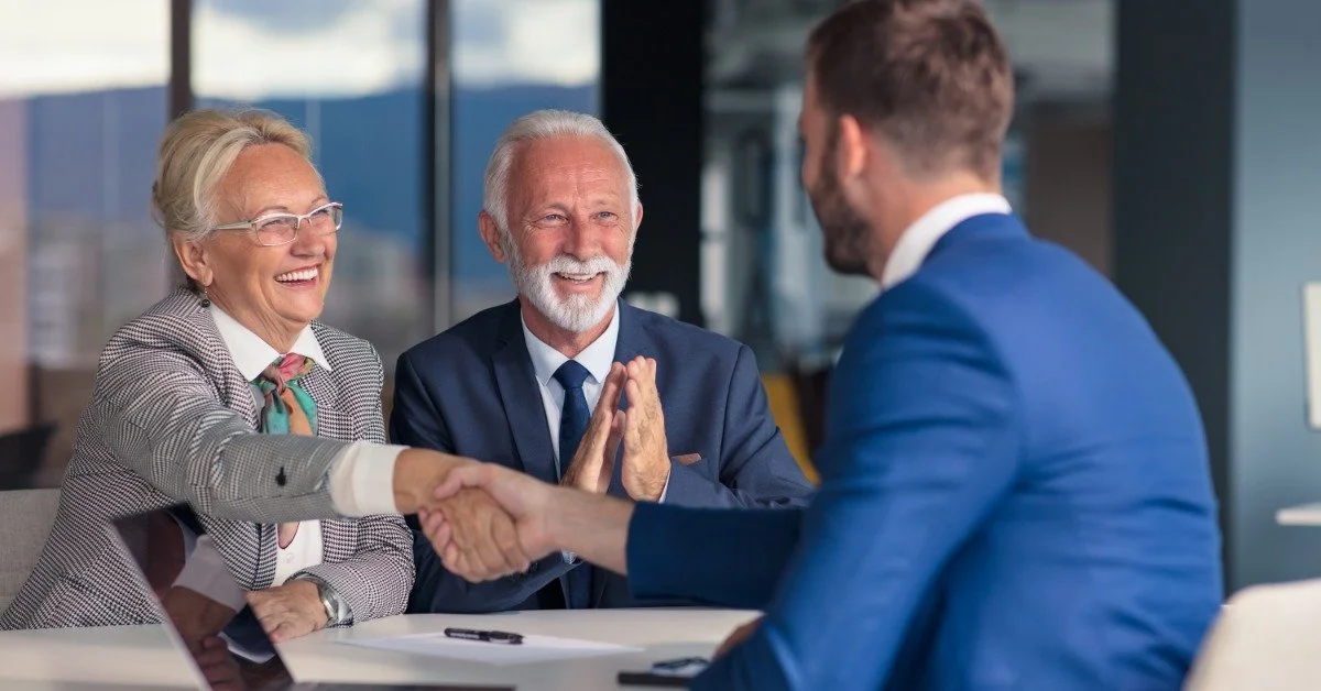 A senior couple shakes hands with a estate planning attorney during a meeting in a modern office setting.