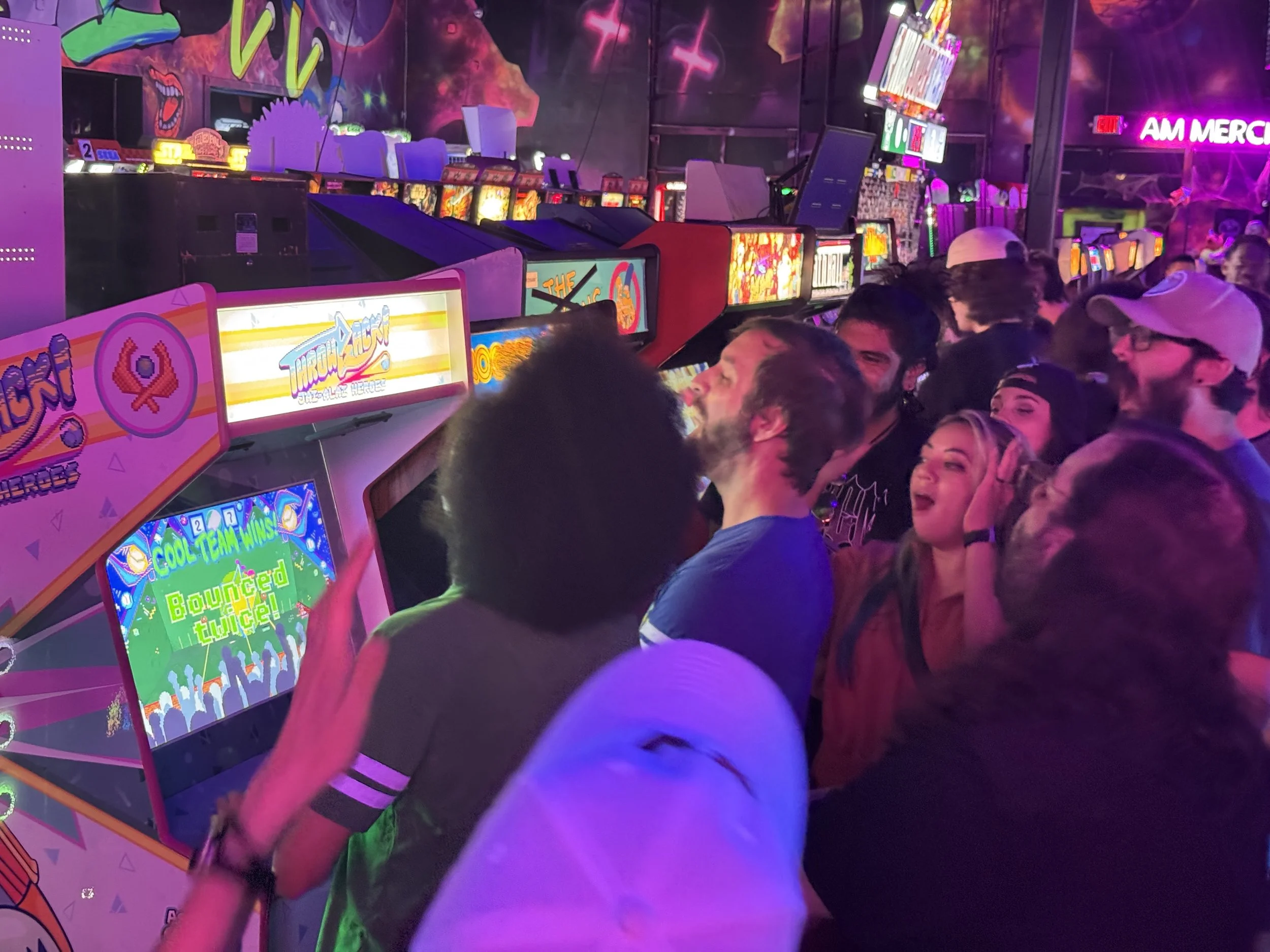 People playing pinball arcade games in a colorful, neon-lit room.