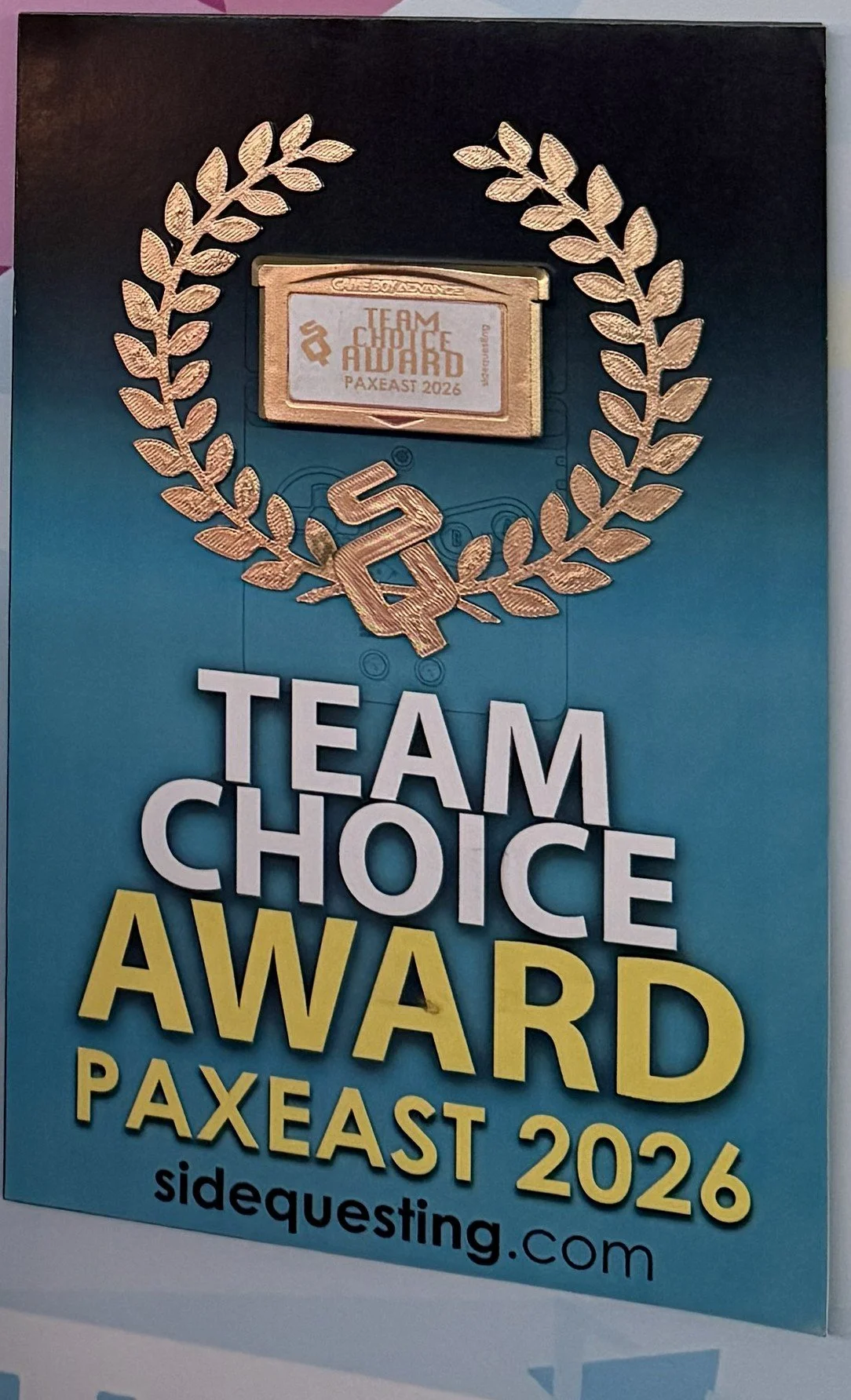 Poster for the 2026 PAXEast gaming event featuring the Team Choice Award with a laurel wreath, a gold and silver trophy, and text including 'Team Choice Award', 'PAXEast 2026', and the website sidequesting.com.